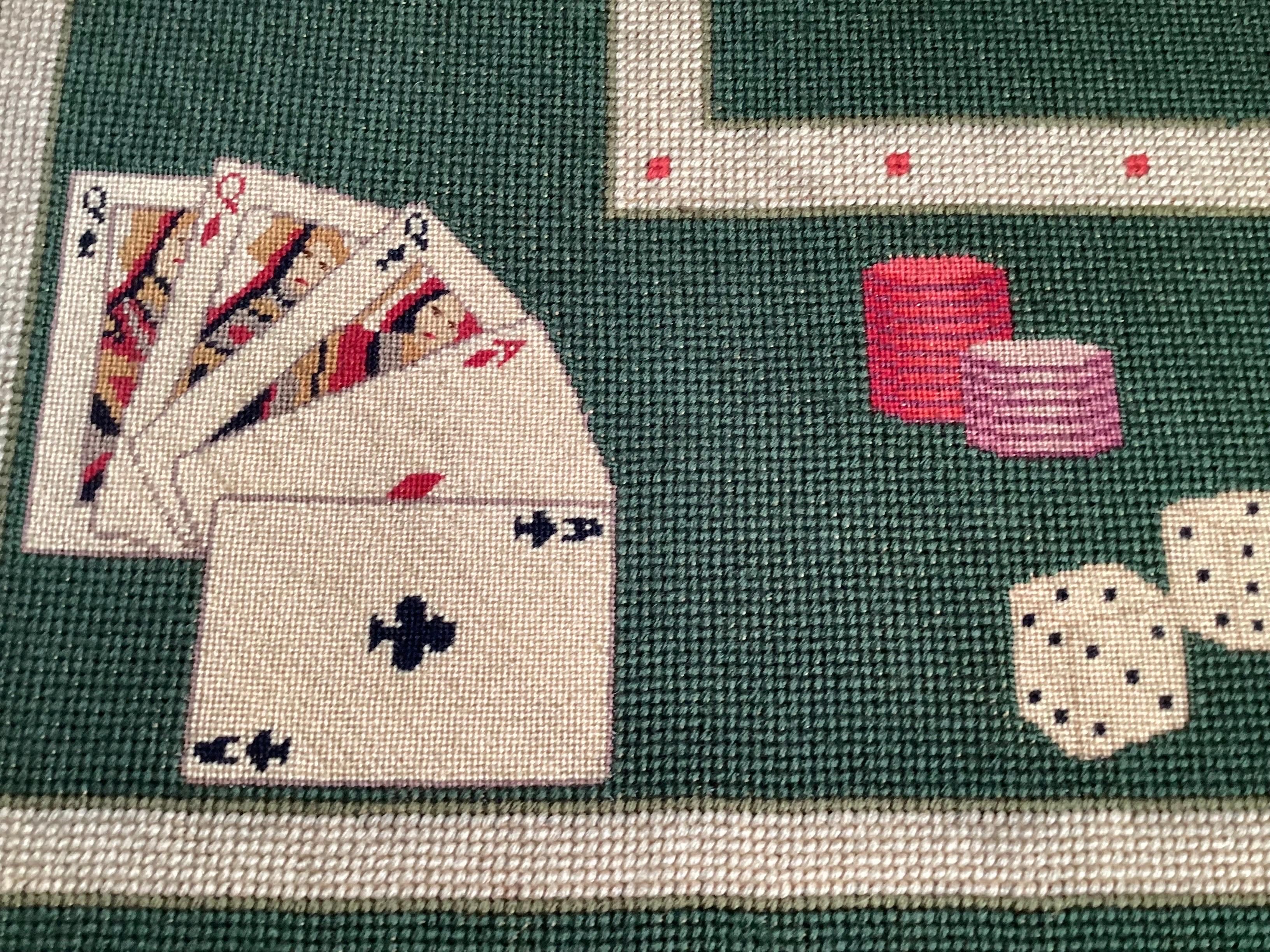 A whimsical wool needlepoint framed table cover with a gambling and sporting theme. The green background with cards, horses, dice and poker chips framed all along the center. There is some signs of age and at one corner a thin spot to the wool.