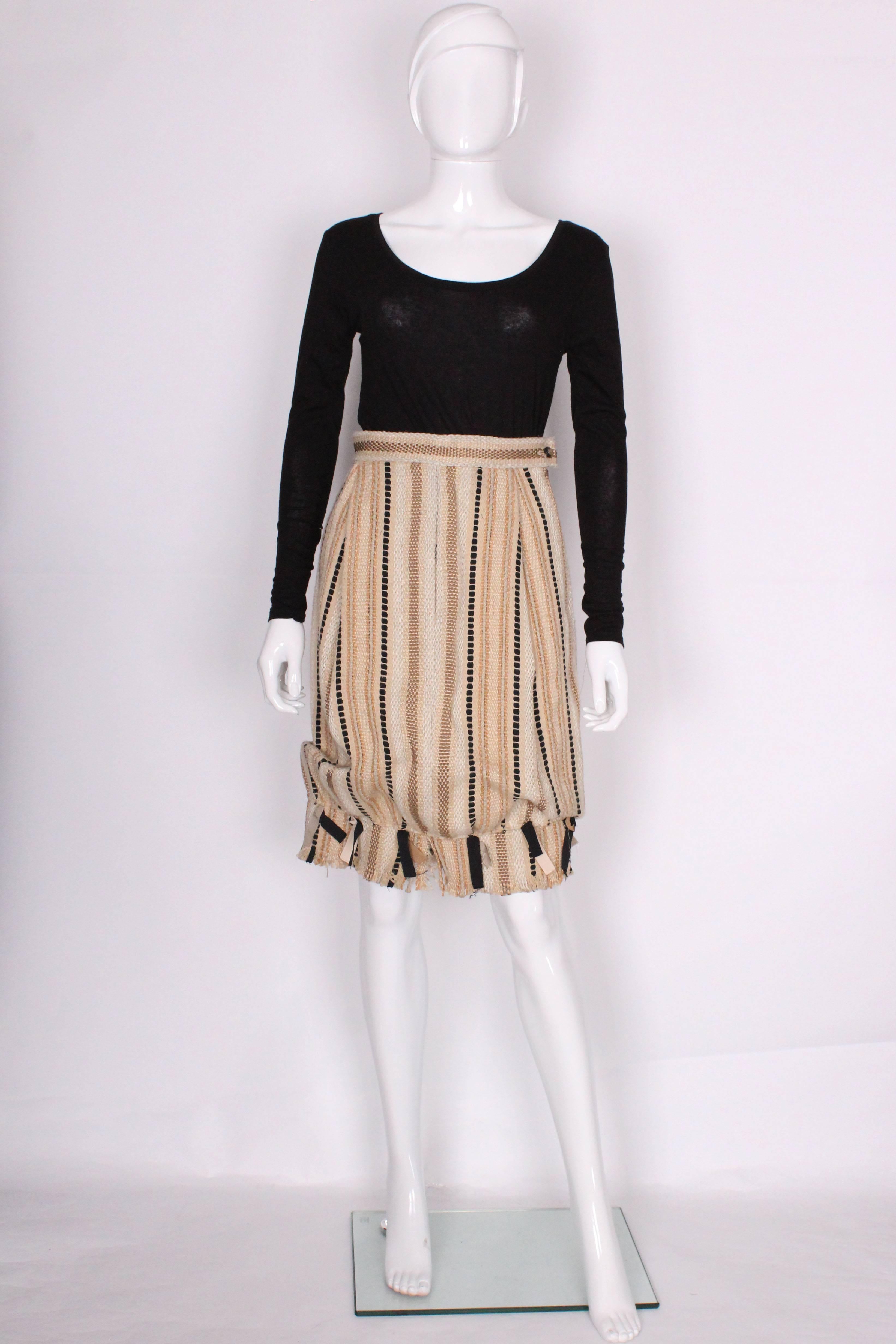 A great skirt by Yves Saint Laurent, Rive Gauche.This skirt is a bubble shape with a 3 1/2'' frill with ribbon detail at the hem. The fabric is a woven mix of linen, jute and acetate, in a biscuit colour background with gold, black and ivory