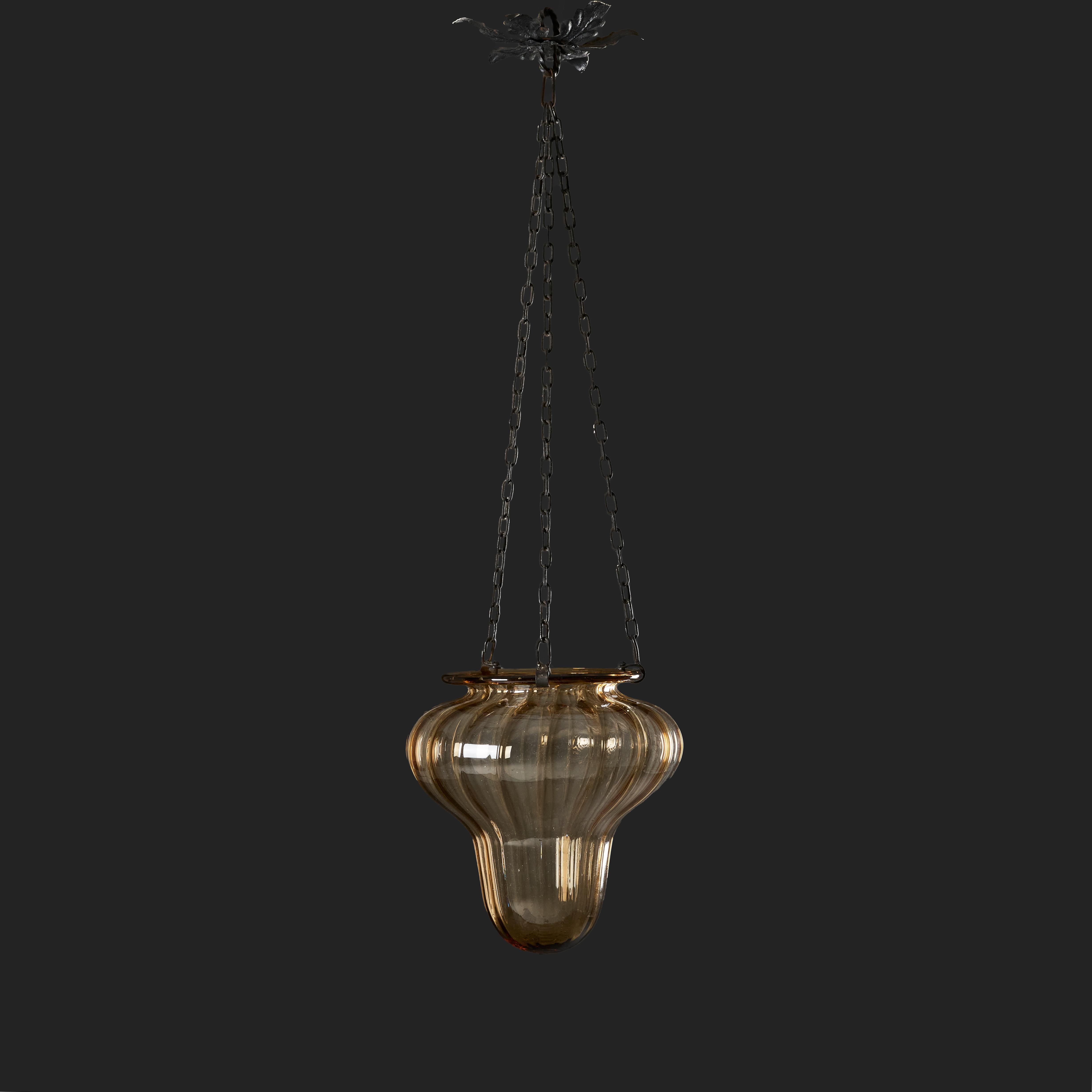 Italia, circa 1940
Lampada a sospensione in vetro ambrato di Murano della metà del XX secolo, a forma di goccia, sostenuta da tre catene con rosone in foglie di tiglio.

Altezza totale fino al rosone del soffitto  84.00cm
Altezza del vetro  