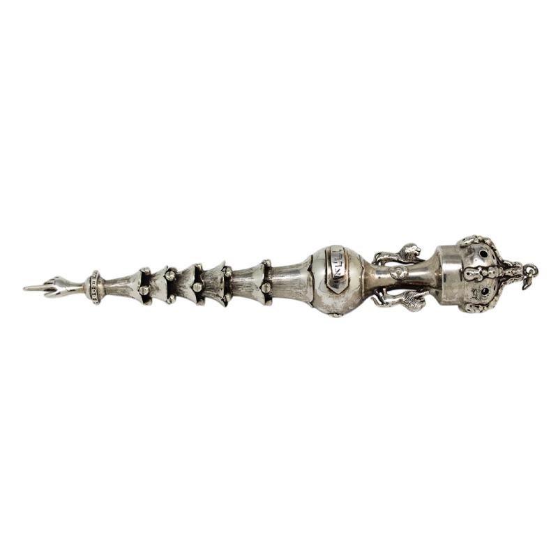 Questo Yad d'argento del XX secolo è un eccezionale esempio di artigianato giudaico, caratterizzato da un design intricato ed elegante. Il manico affusolato è ornato da una serie di bracciali scanalati e sovrapposti, ciascuno impreziosito da una