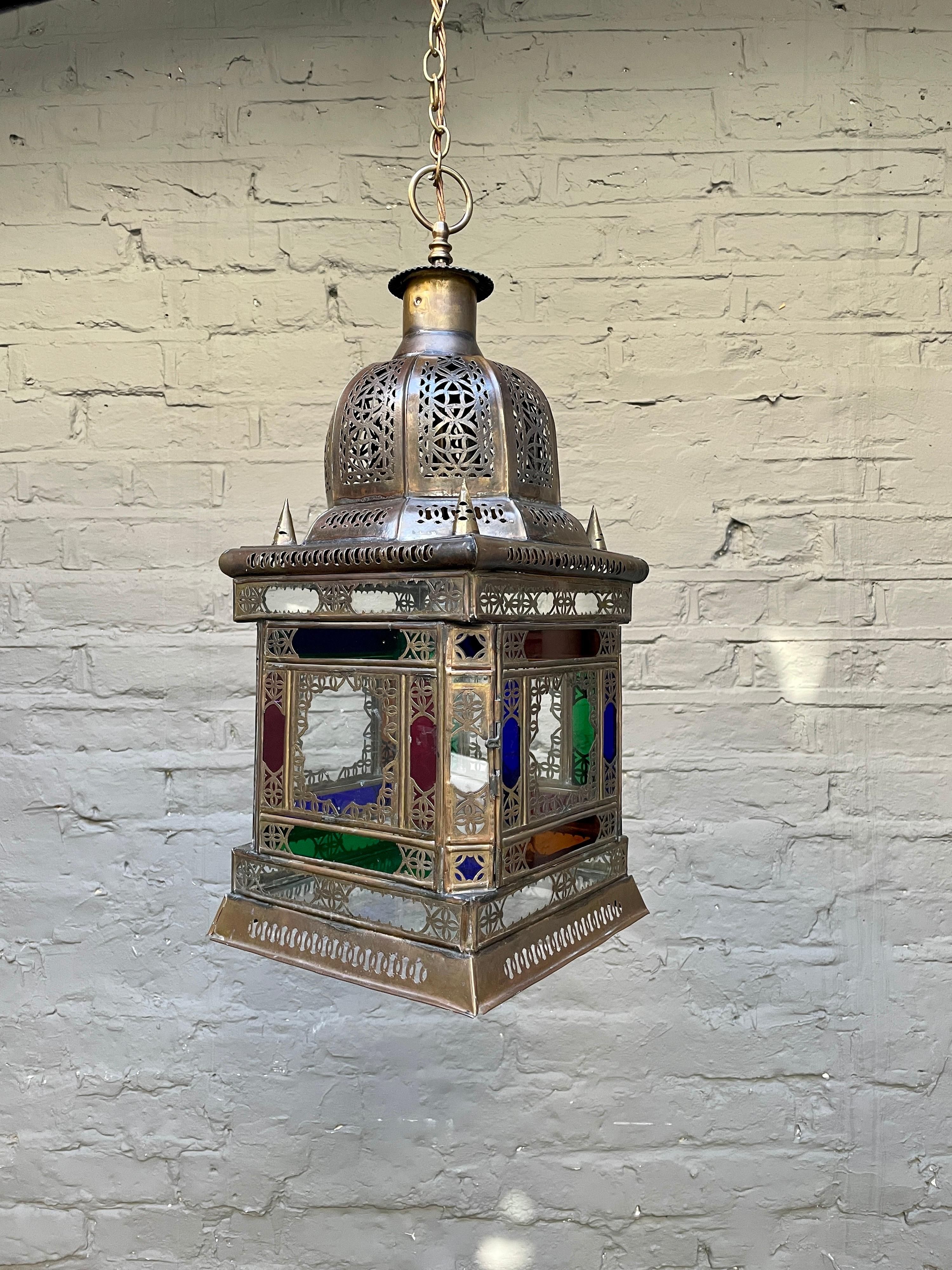A Moroccan lantern, in intricately cut and pierced brass with coloured glass and clear panels.