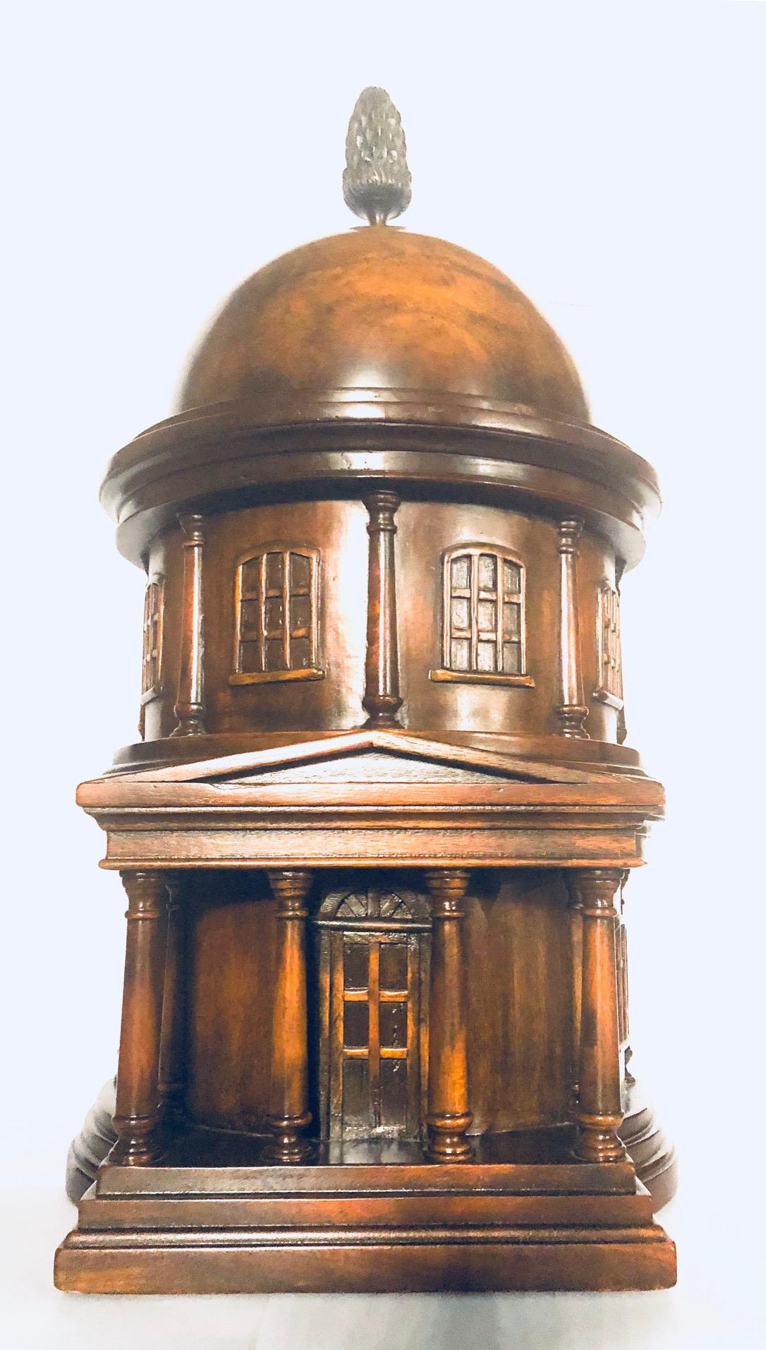 In three parts, the domed roof with bronze pine cone finial lifting off to concealed compartment, the second section lifting off to further compartment, the front with angular pediment to central door with column either side, windows to the second
