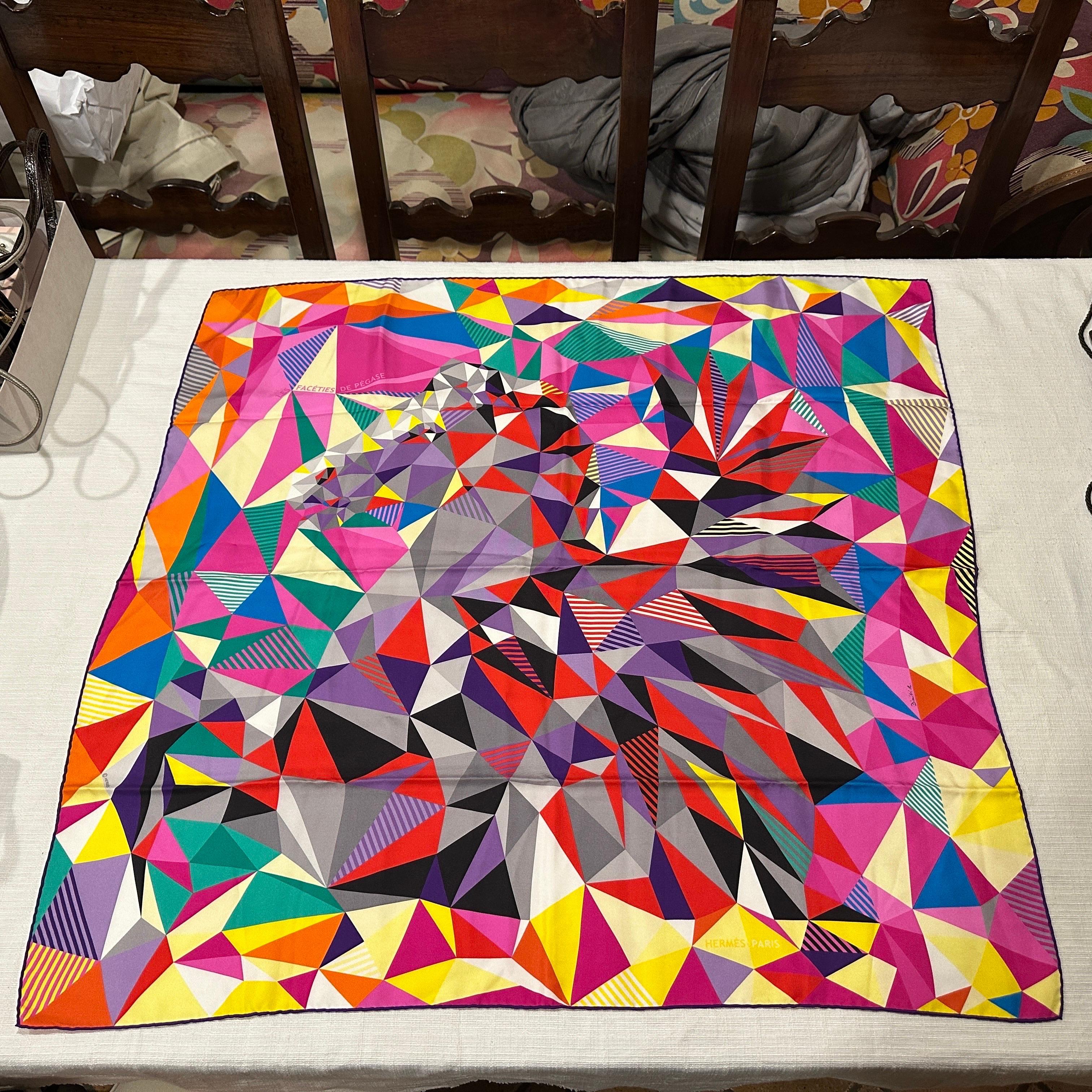 This vibrant silk scarf by Hermès, Les Facéties de Pégase designed by Dimitri Ribaltchenko, is a masterpiece of geometric artistry. The scarf features a kaleidoscope of colorful, triangular patterns that create a dynamic and visually striking