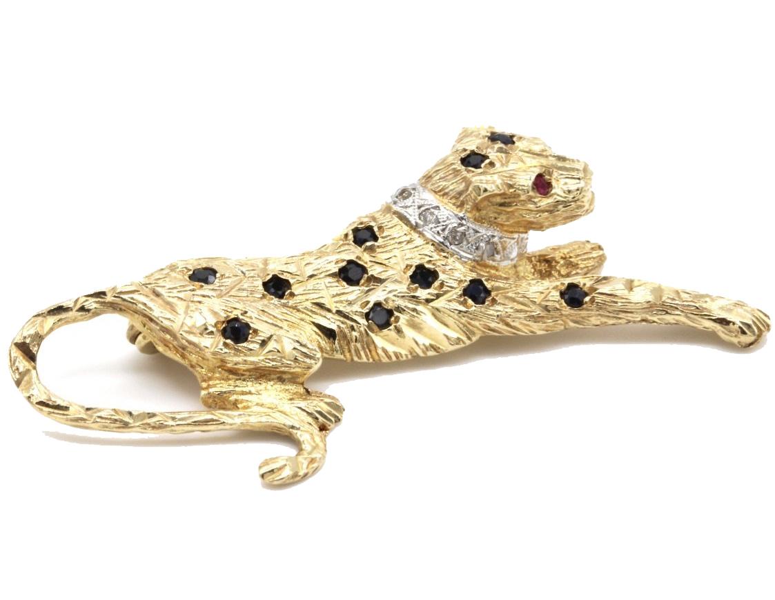 A 9 Kt yellow gold Cartier style jewel encrusted panther tie pin / lapel brooch.
The finely modeled body of the panther set with eleven sapphires, the eyes formed by two rubies and the white gold collar with four diamonds.
Hallmarked Birmingham UK  