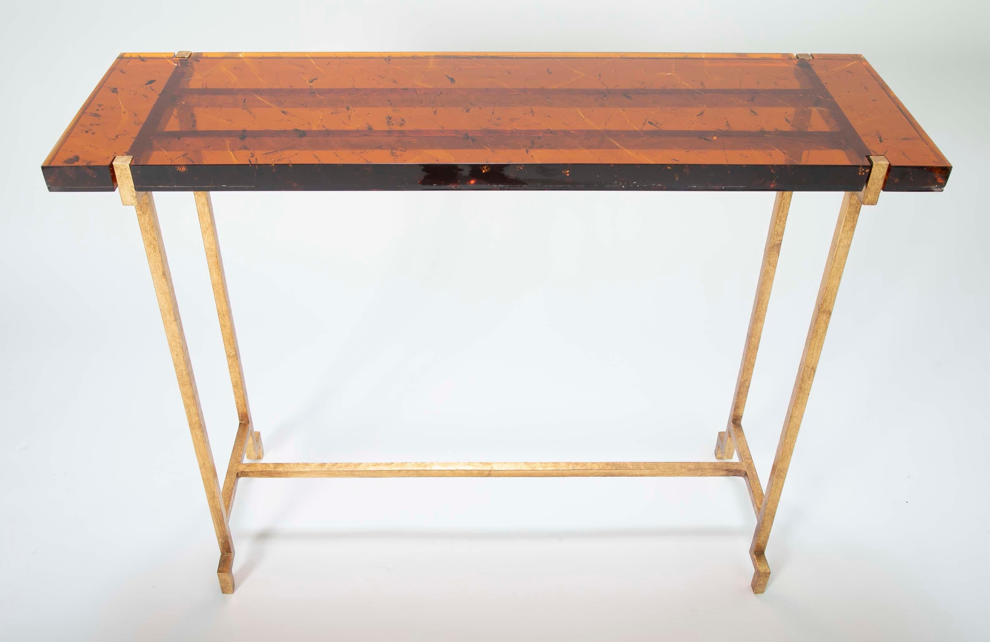 A gilt steel console table with amber toned Lucite top. The top was designed to have fissures imbedded throughout the Amber Lucite.