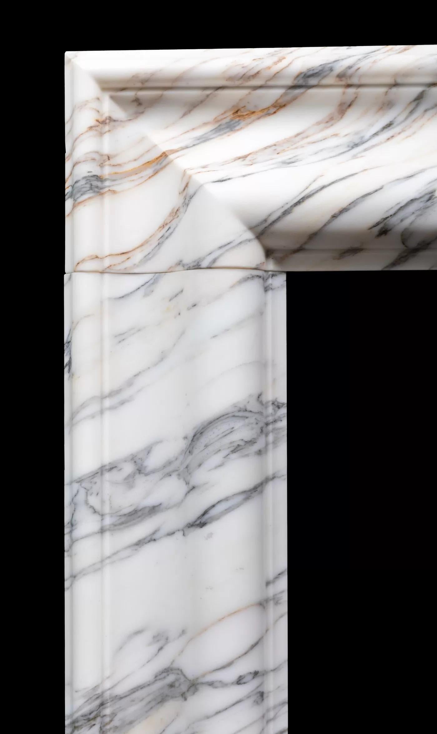 Eine mittelgroße Kaminumrandung im Bolection-Stil aus italienischem Arabescato-Marmor von Ryan & Smith.

Ein klassischer Kamin im Bolection-Stil mit einem sanft geformten Rahmen auf schlichten, quadratischen Sockeln, der aus sorgfältig ausgewählten