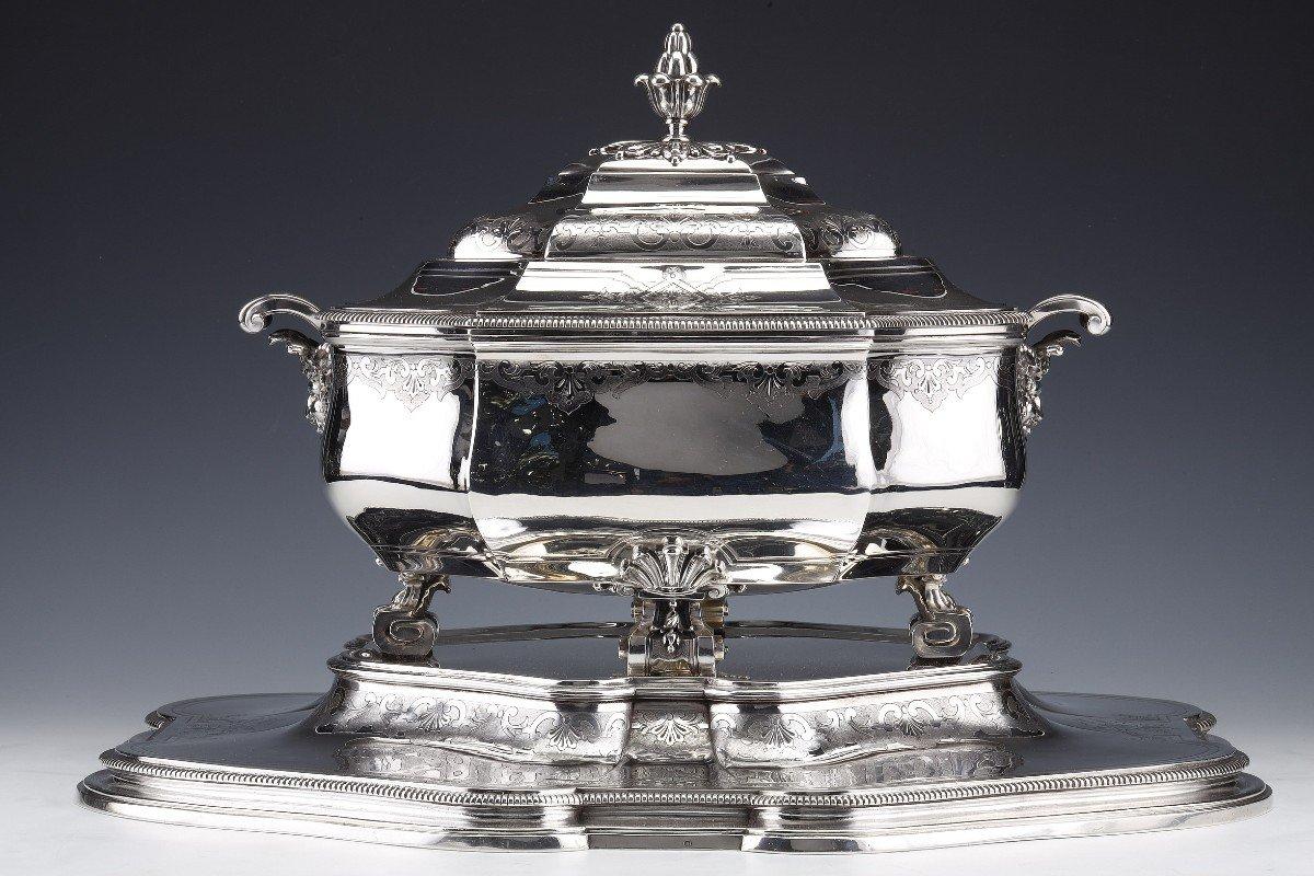 Importante centro de mesa de plata maciza representado por una sopera tapada montada sobre cuatro patas sinuosas y colocada sobre su bandeja. Ricamente decorada con grabados de Bérain, ribete de gallones, las empuñaduras laterales en forma de