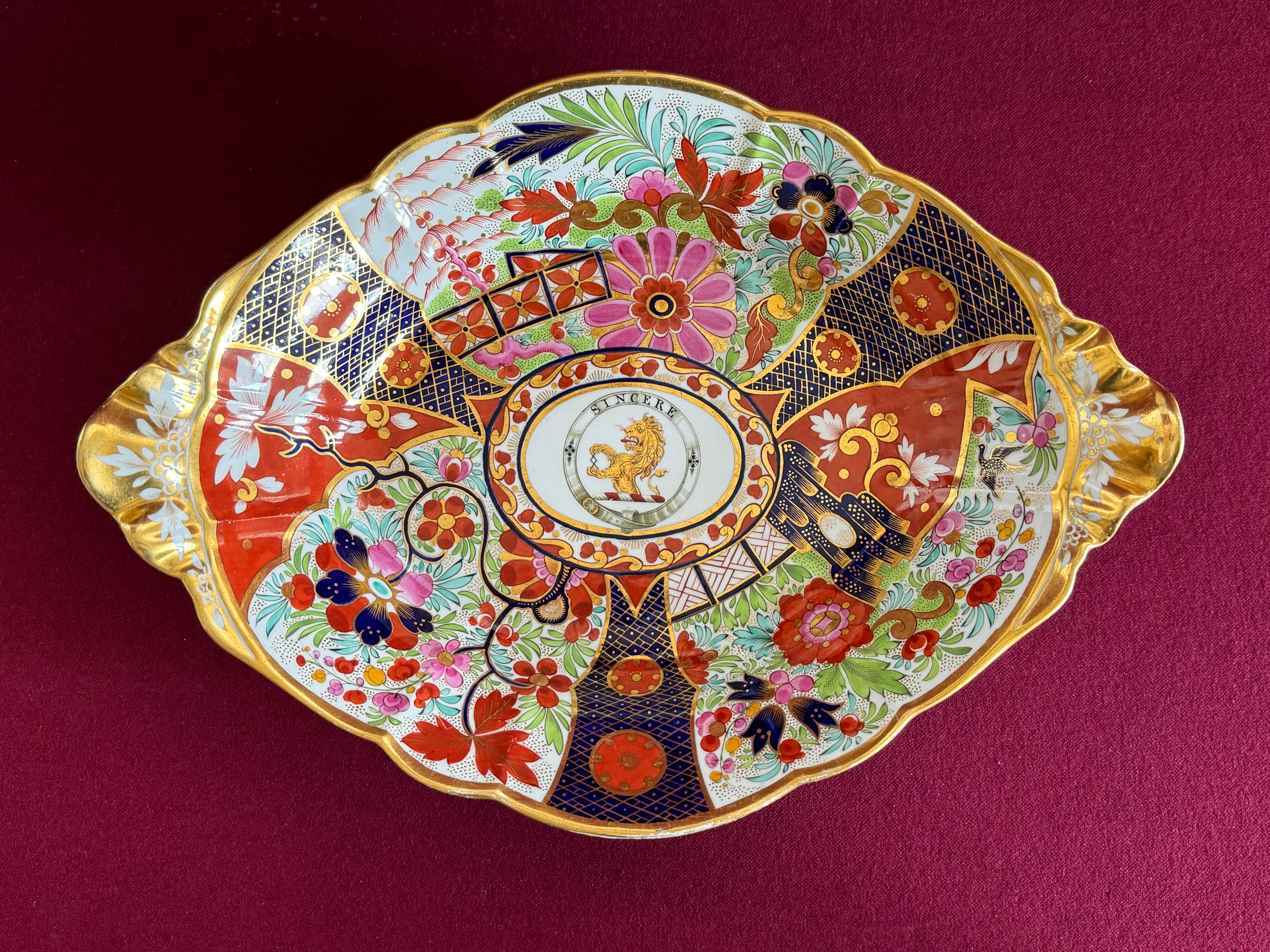 A large Barr, Flight & Barr Worcester Porcelain Centrepiec c.1804-1813 painted in a rich ‘Japan‘ pattern, with elaborate panels of a fenced garden, pierced rockwork and flowering branches separated by blue diaper bands. In its centre is the crest of
