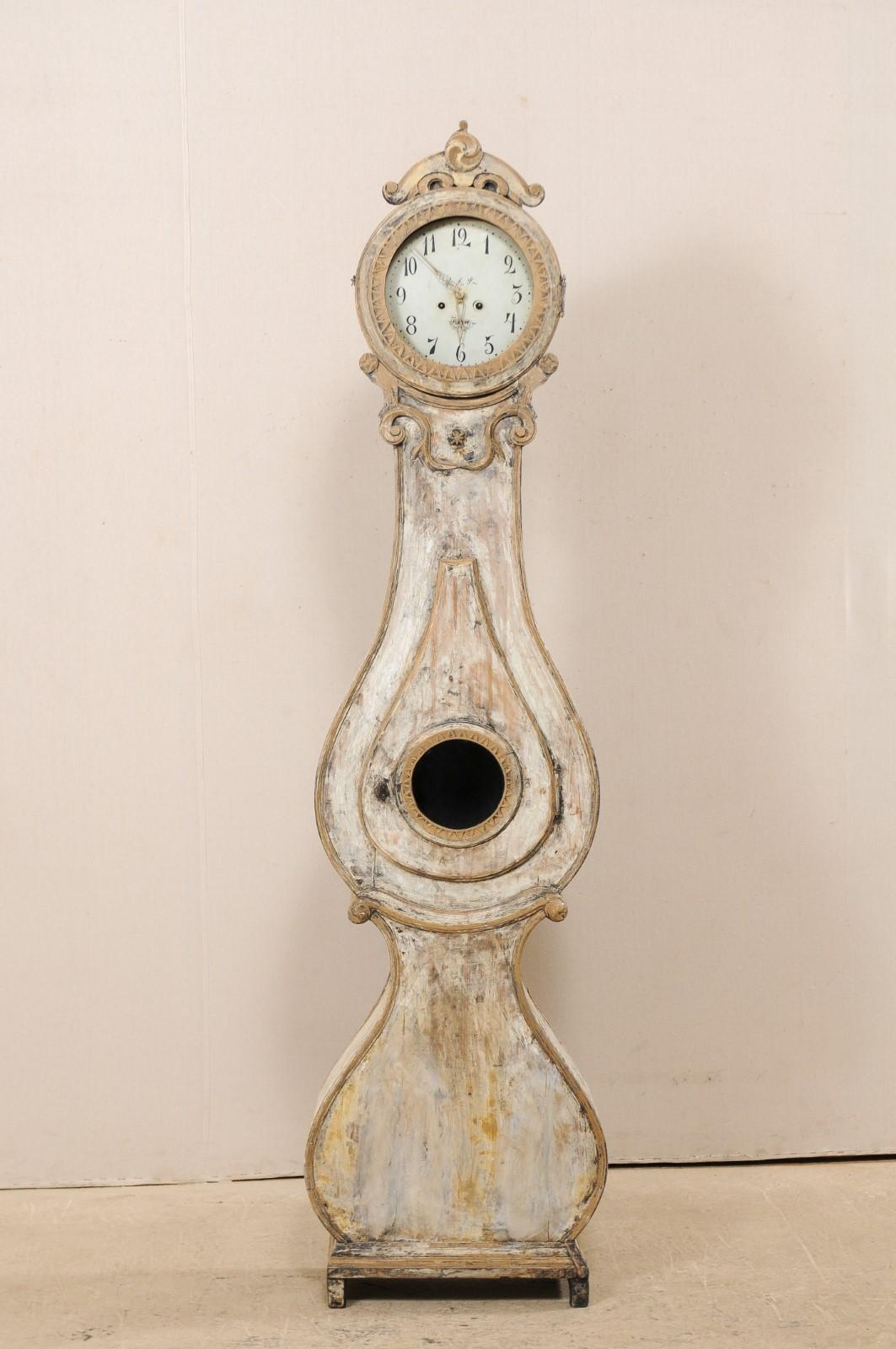 A 19th century Swedish Fryksdahl grandfather clock. This antique Fryksdahl clock from Sweden features a beautifully raised and carved crest, petite flowers on either end of a swag molding and volute accents at the neck with a central star. The