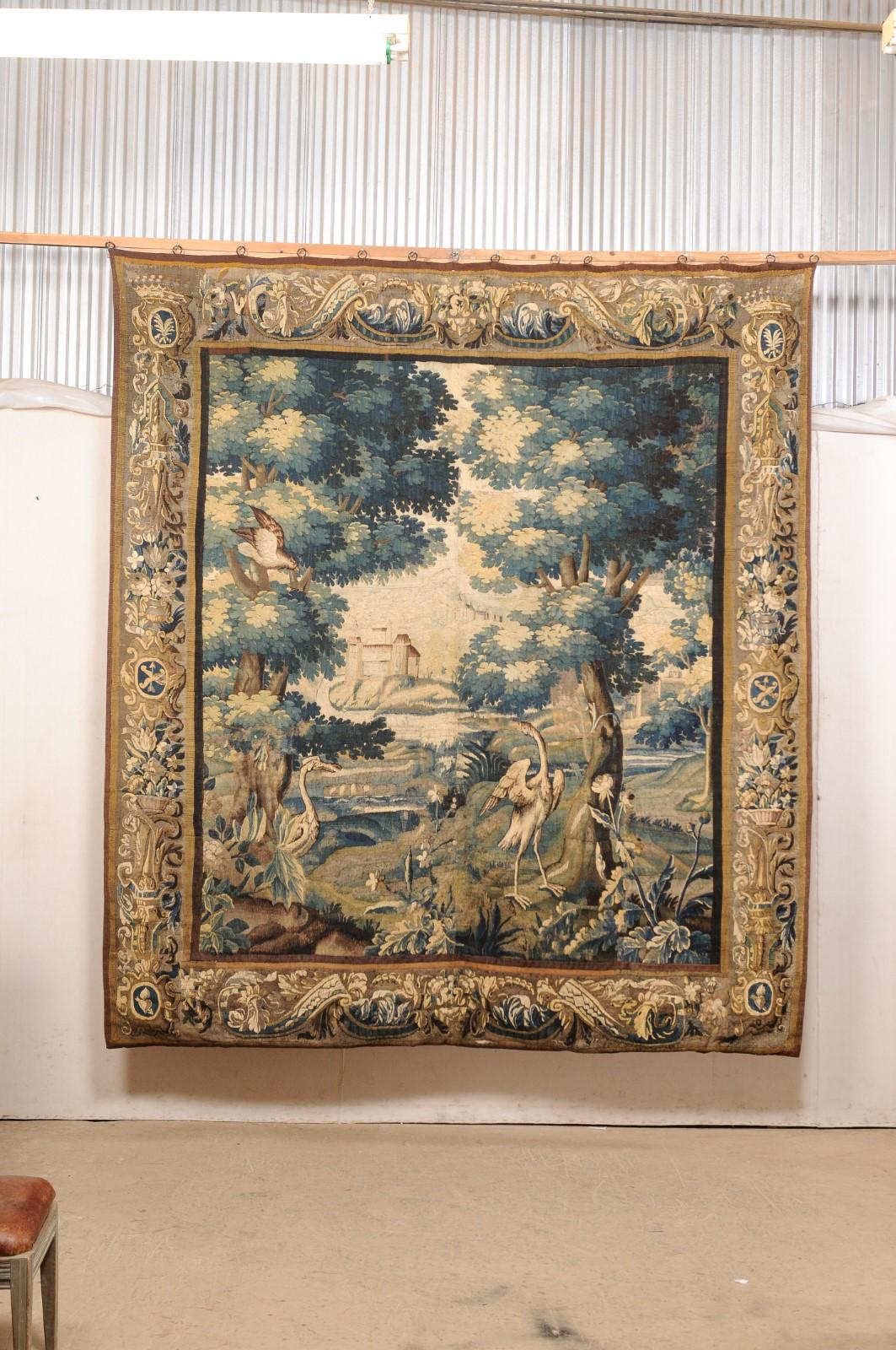 A Flemish large-sized hand-woven verdure tapestry from the 18th century. This antique textile from Belgium, approximately 8 feet 4 inches wide by 9 feet 3 inches tall, is an artful depiction of birds within a scenic forested landscape setting and