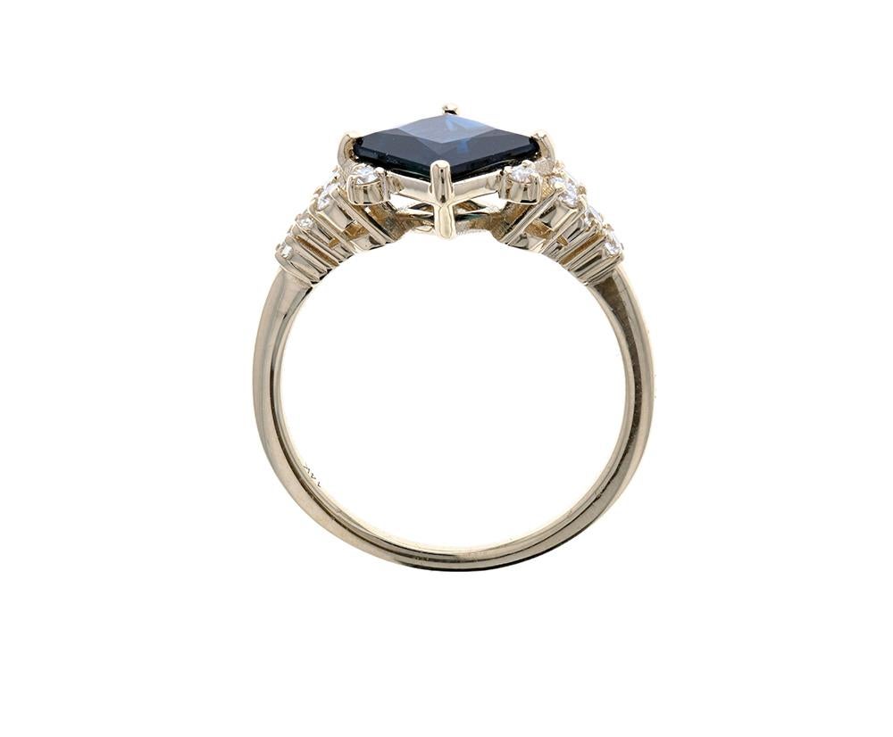 This beautiful classically blue princess cut sapphire has been set in yellow gold and accented by 12 delicate white round diamonds to elevate the look.  A stunning color on this center stone is made even more illustrious by the yellow gold color of