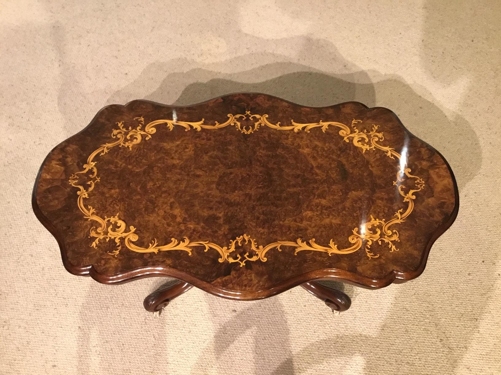 A beautiful burr walnut Victorian shaped coffee table. Having a shaped top in beautifully figured burr walnut with a floral marquetry inlaid border. Supported on a 'basket' walnut base with carved cabriole supports and brass and porcelain castors.