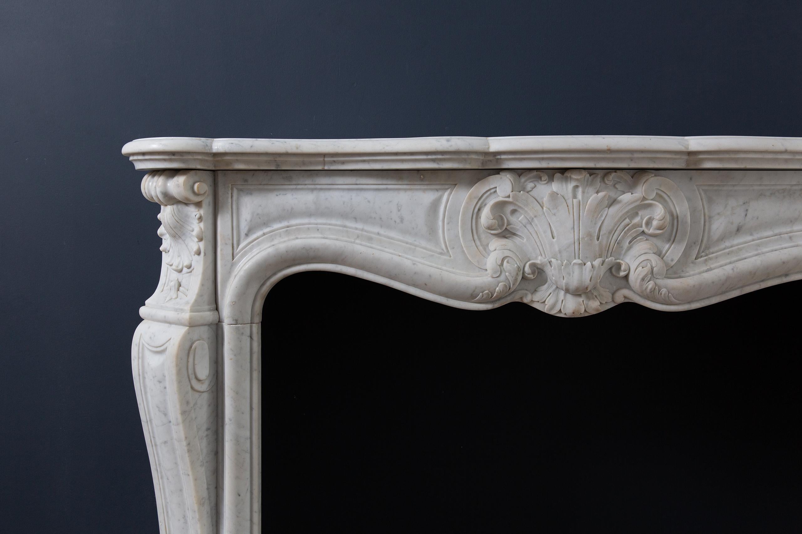 Luxurious antique French front fireplace in Carrara marble. This beautiful fireplace has a beautifully detailed front with a large shell. The consoles are at an angle. The side plates of this fireplace are not only provided with a beautiful brass