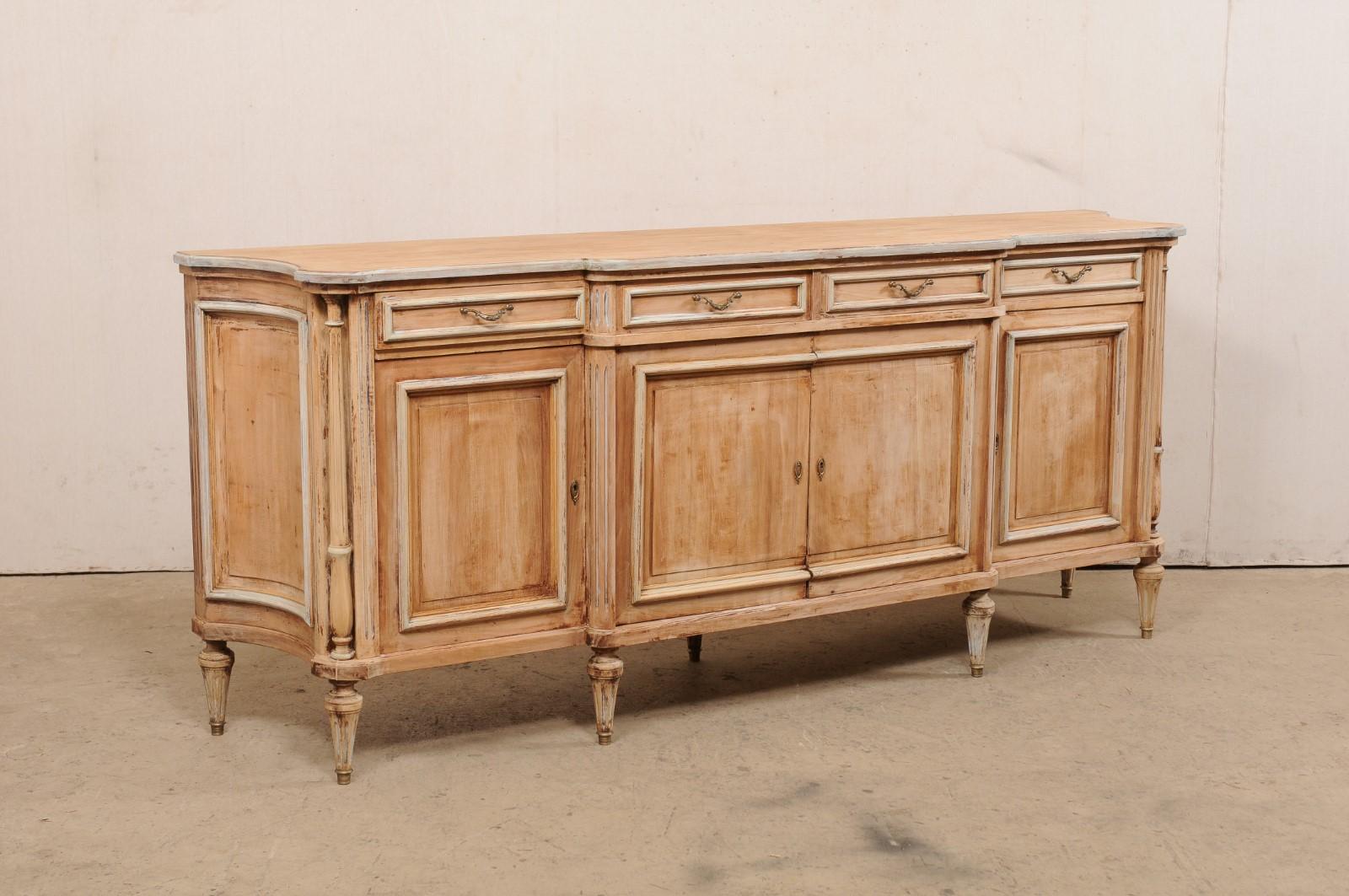 A French carved wood sideboard, with column accents and bleached finish, from the mid 20th century. This mid-century buffet console from France has a curvaceous form with subtle break-front and concave appearance at sides. Four panel-front drawers