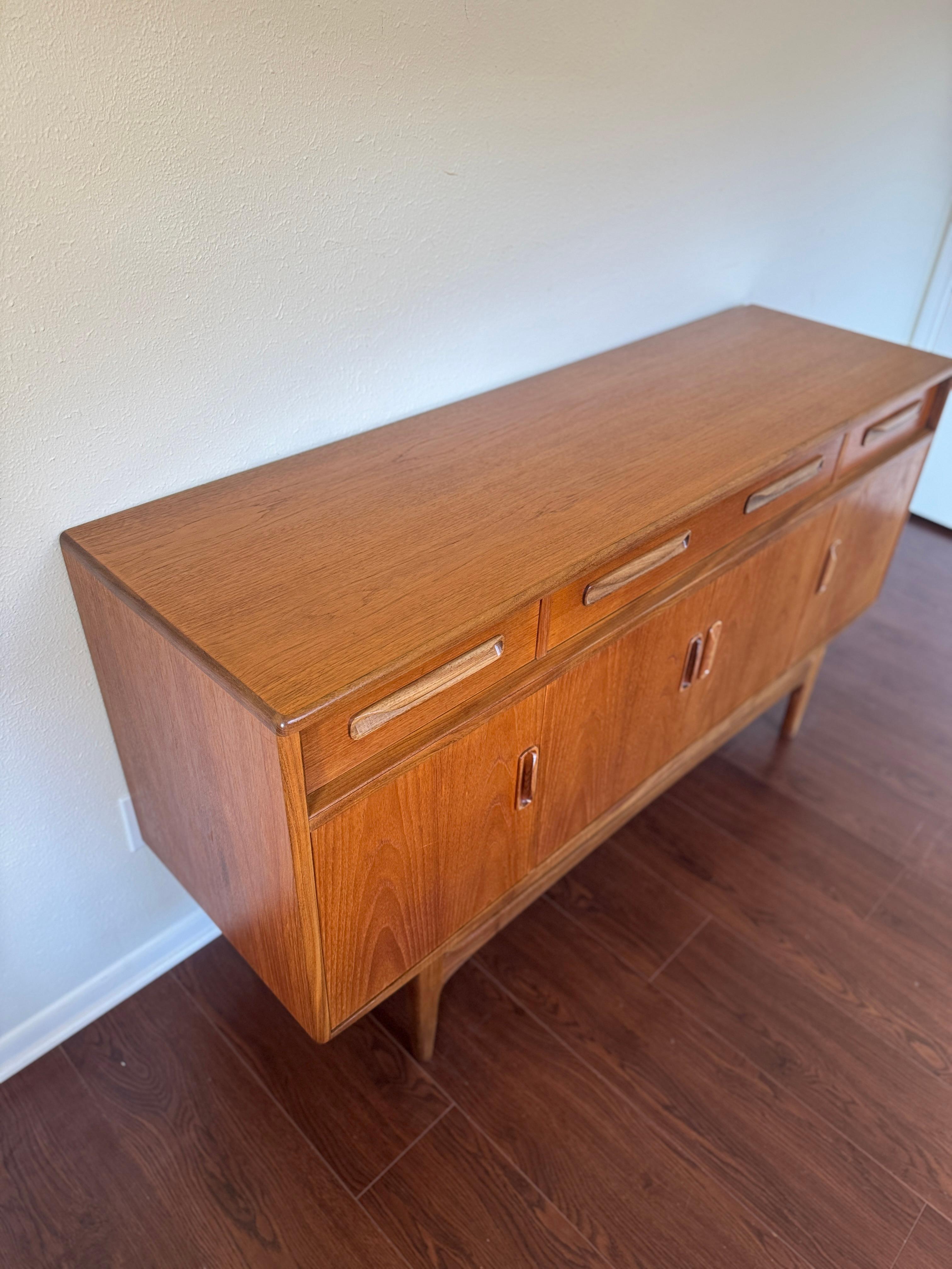A beautiful G Plan sideboard signed by Ib Kofod Larsen, circa 1960s. It is an exceptionally well-balanced design with dark Afromosia sculpted handles and trim contrasting against the teak veneer. It sits upon an elegantly curved stretcher and