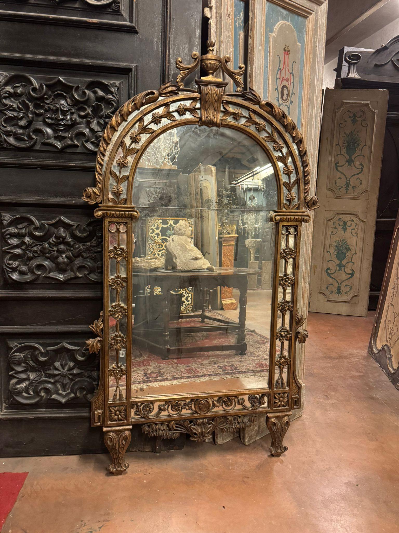A highly valuable antique mirror in Neoclassical style with a gilded and carved frame. It features a vertical rectangular shape with an arched top. The mirror has feet for standing but could also be hung on a wall.
The frame is finely carved in