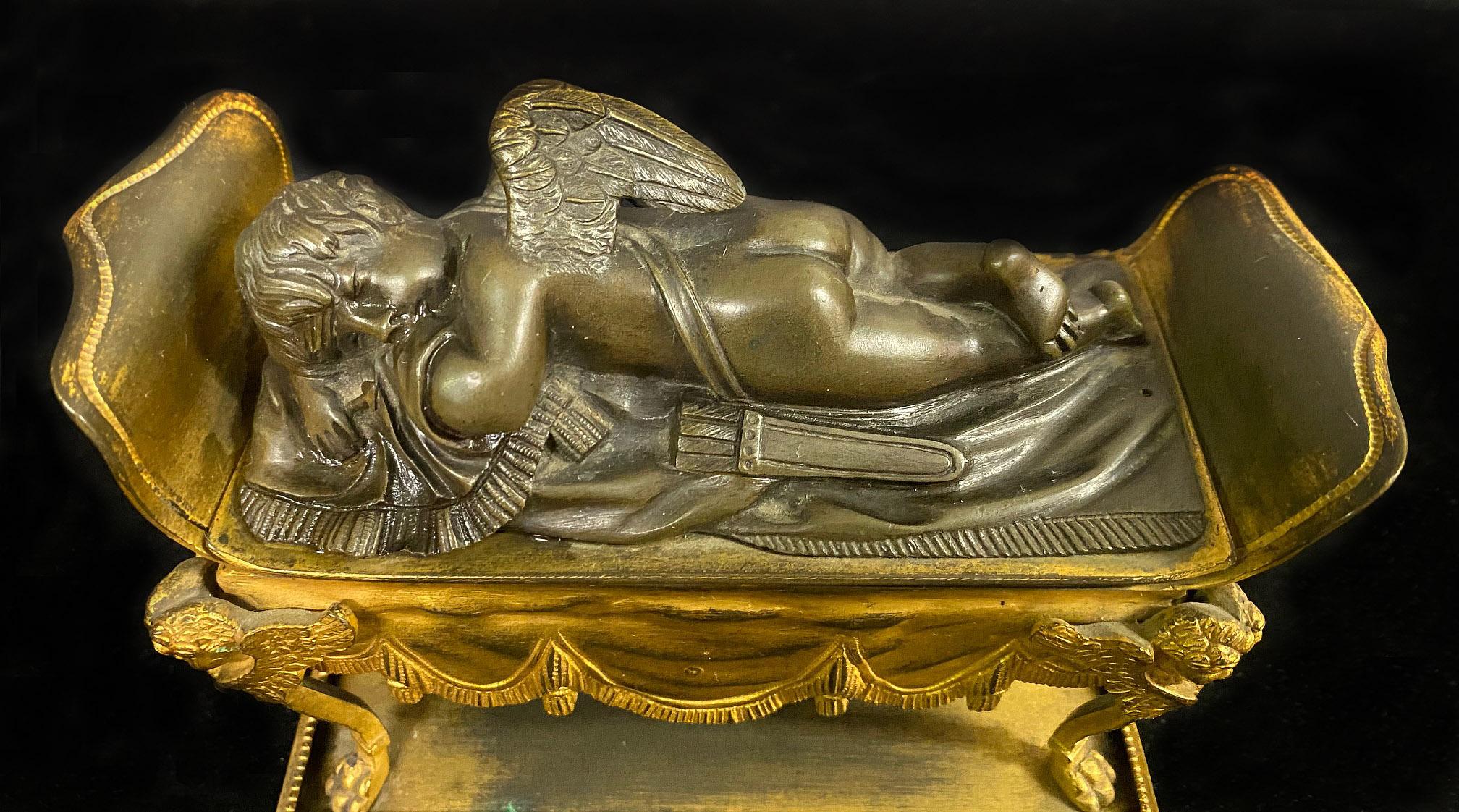 A beautiful late 19th century gilt and patina bronze inkwell

Depicting a bronze sleeping cherub lying on a gilt bronze settee, opening up to two ink holders.