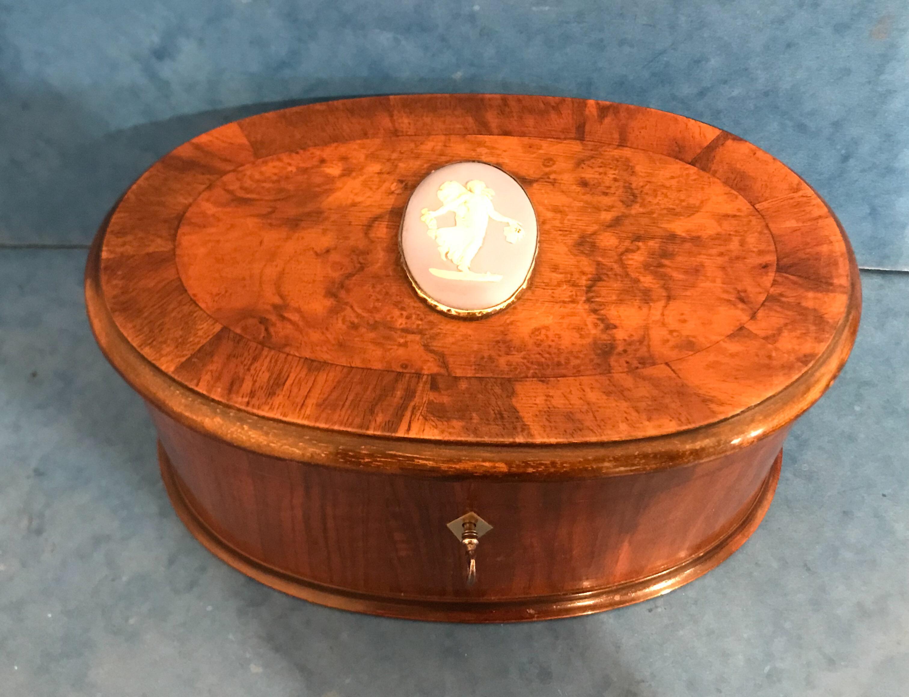 This is a beautiful late Victorian 1900, crossbanded walnut oval box, it has a wedge wood mounted lid, it has it’s original blue velvet interior and a working lock and key. It measures 24 by 15.5 and stands 11cm high, it’s a stunning box.