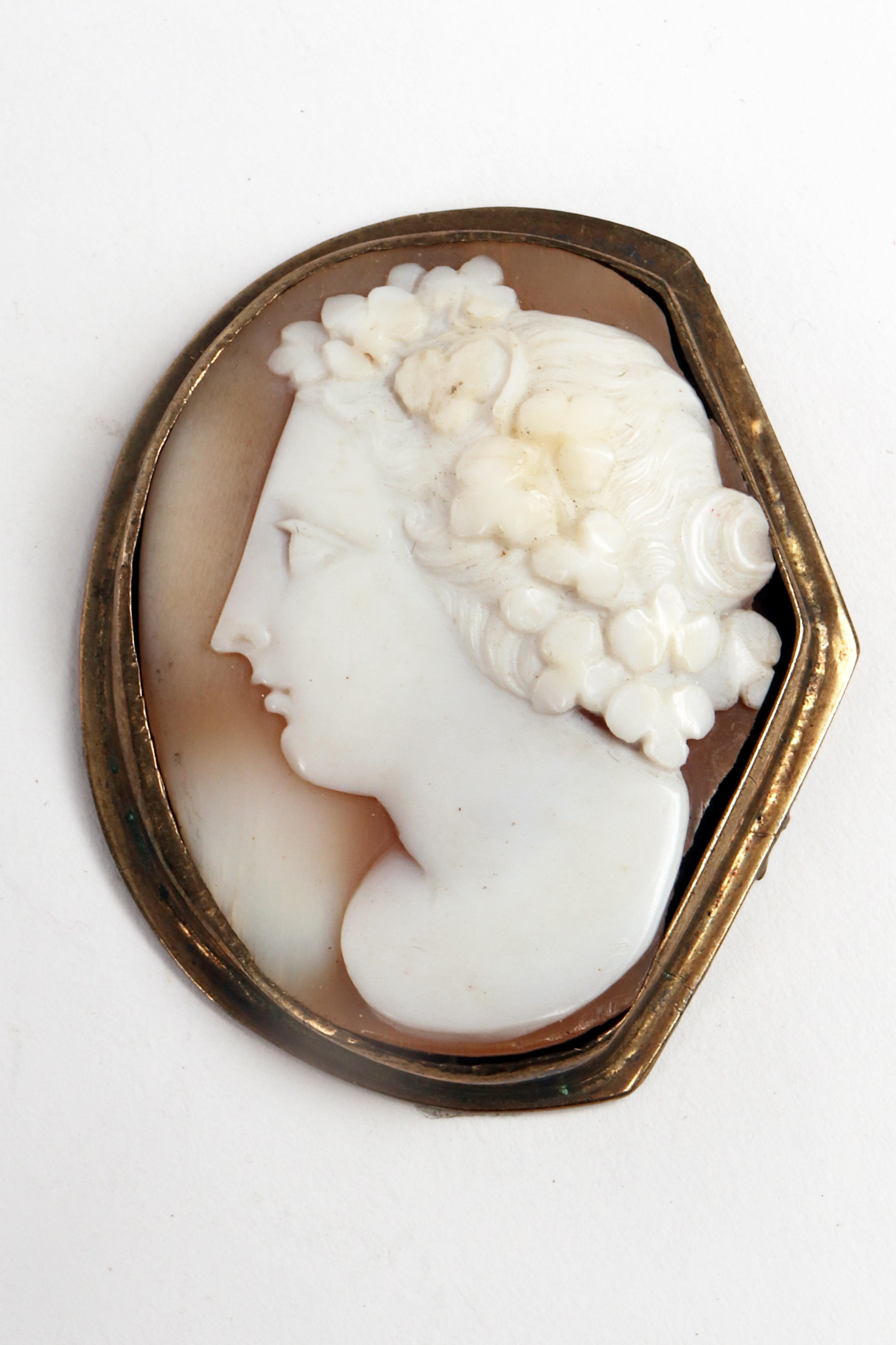 Shell cameo with an asymmetrical edge, mounted in gold metal depicting a neoclassical female profile with a rich hairstyle decorated with a garland of flowers. The back has traces of attachments to a double chain, for use as a choker.
England end of