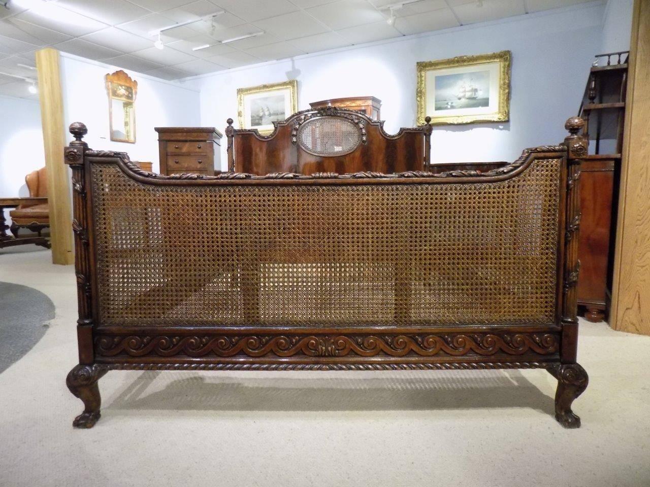 A beautifully carved mahogany Edwardian Period double bed in the French taste. The head board having a fine ribbon and swag carved crest and acanthus carved detail to the frame, having a central oval caned panel, turned acorn finials and trailing