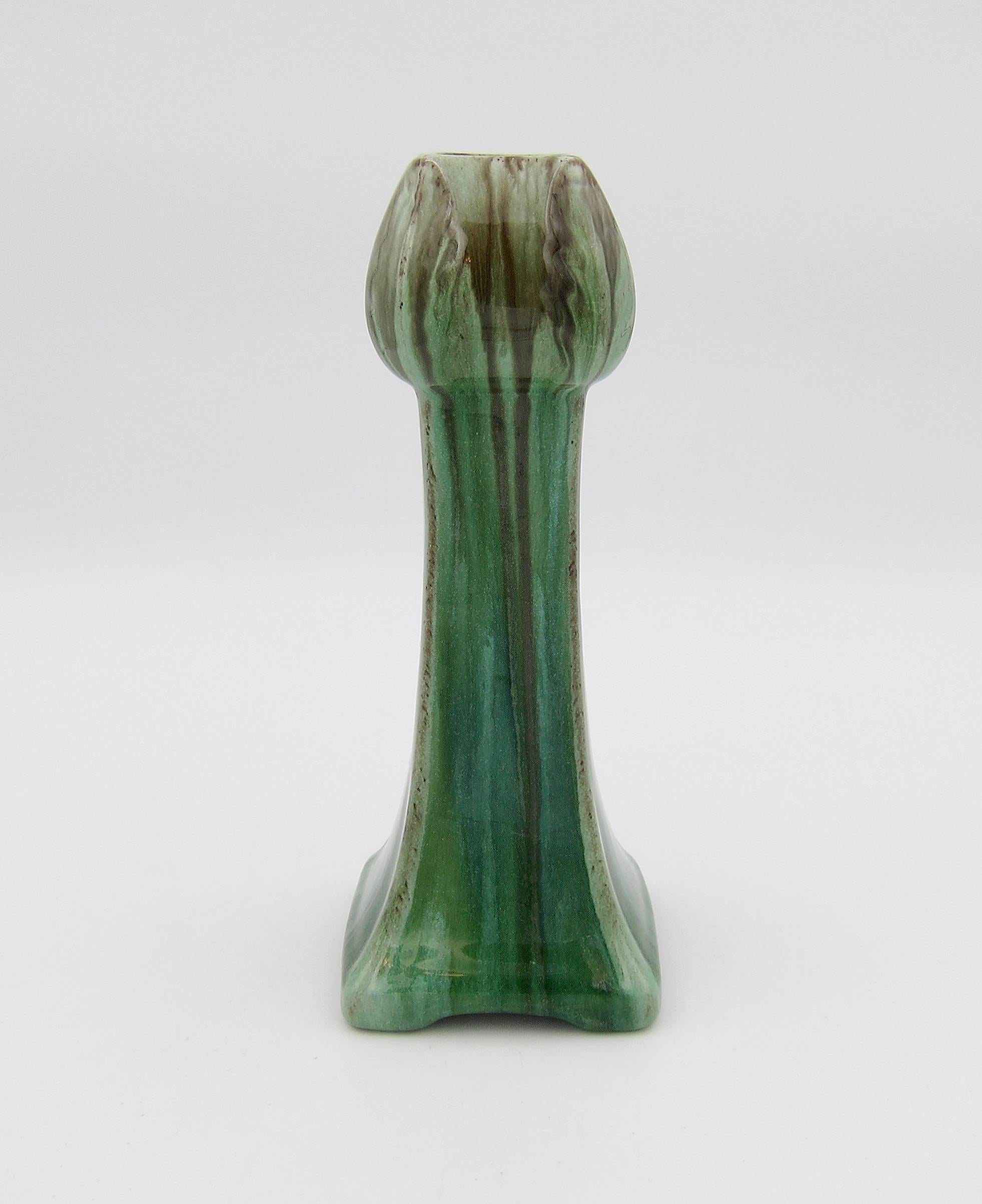 A vintage vase in the Art Nouveau style made in Belgium, circa 1940s. The vessel resembles an abstracted tulip with a flaring foot enveloped in a glossy drip glaze in shades of green with brown accents over a red clay body. The slender vase displays