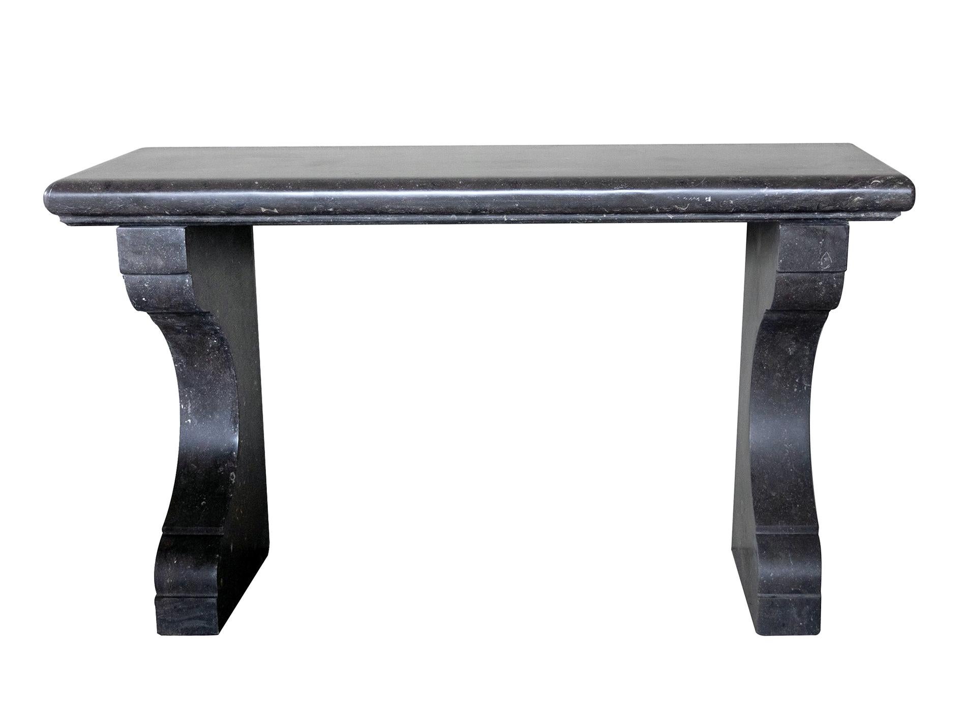 Fabriquée en pierre bleue belge avec une finition adoucie et incrustée de fossiles, la table console est composée d'un épais plateau rectangulaire avec un bord en ogee, le tout reposant sur des supports concaves à volutes. Neuve avec seulement une