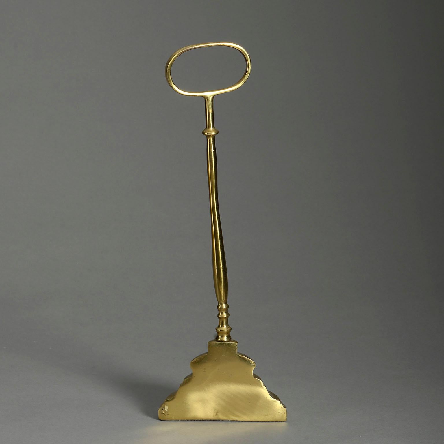 A polished brass doorstop in the Victorian style, the loop handle set upon a turned stem on a shaped bell weight.

  