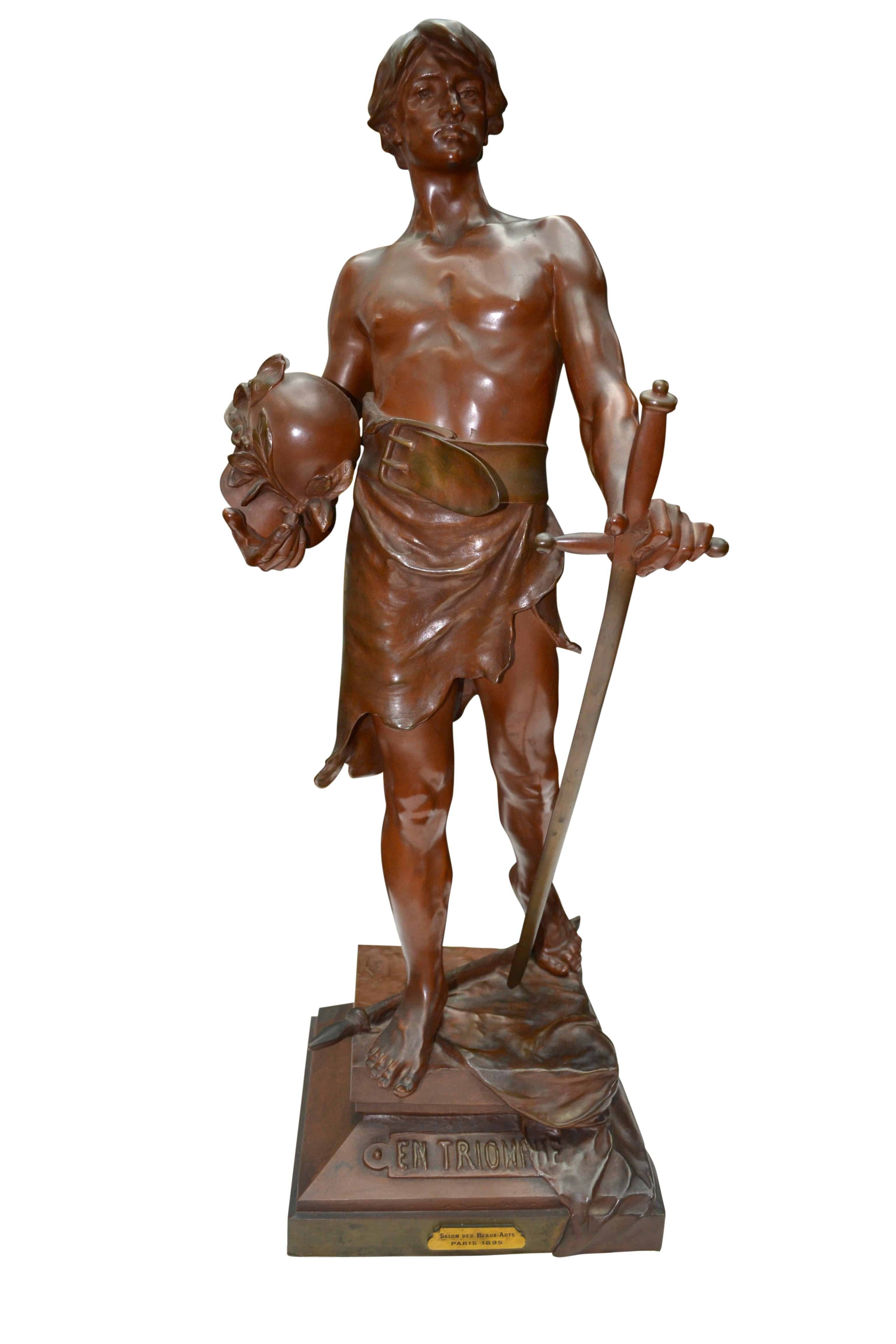 A beautifully cast bronze statue with chocolate color original patination of a standing bare chested warrior youth wearing an animal hide from his waist down held up by a thick buckled belt. In one hand the warrior is holding a helmet, the other is