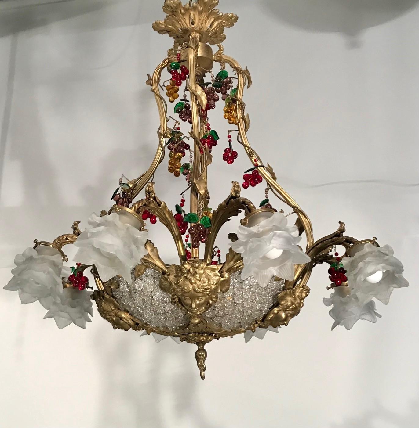 This chandelier has a heme-spherical “bag” formed as florets and eight down-swept lights with opaque flower-form shades interspersed with masques of the young Dionysis/Bacchus, so provides a lot of  potential candlepower. The vinous theme is further