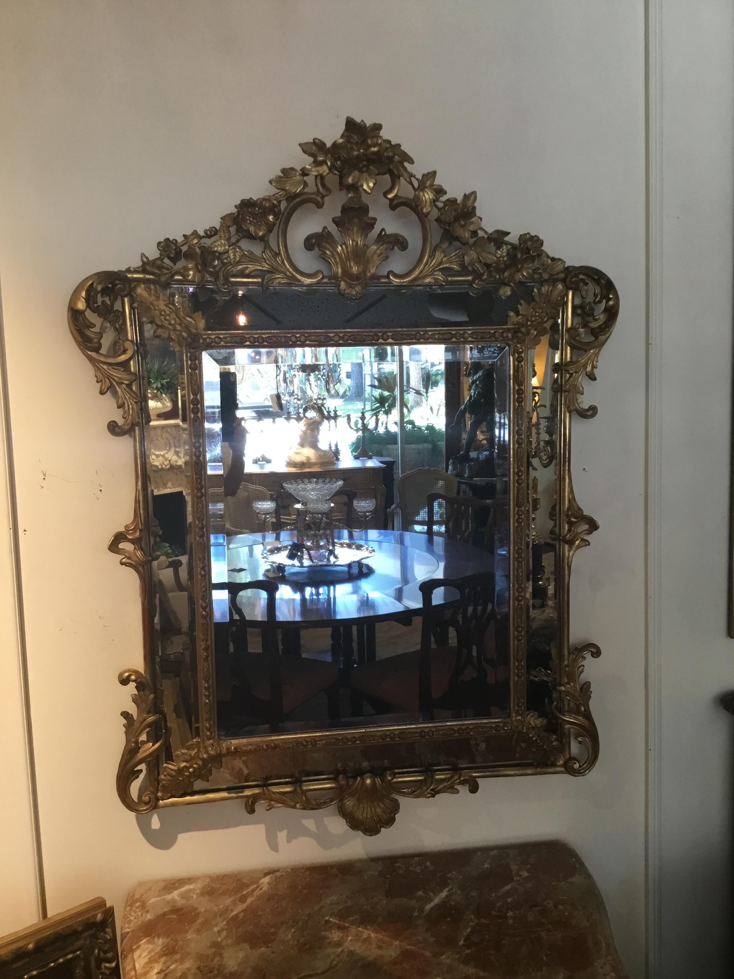 A double framed and double beveled gilt mirror with canted sides. A shell cartouche is centered
at the top and the bottom of this lovely piece. Floral carvings and swags encircle the shell carving.
Curved swags embellish each corner.