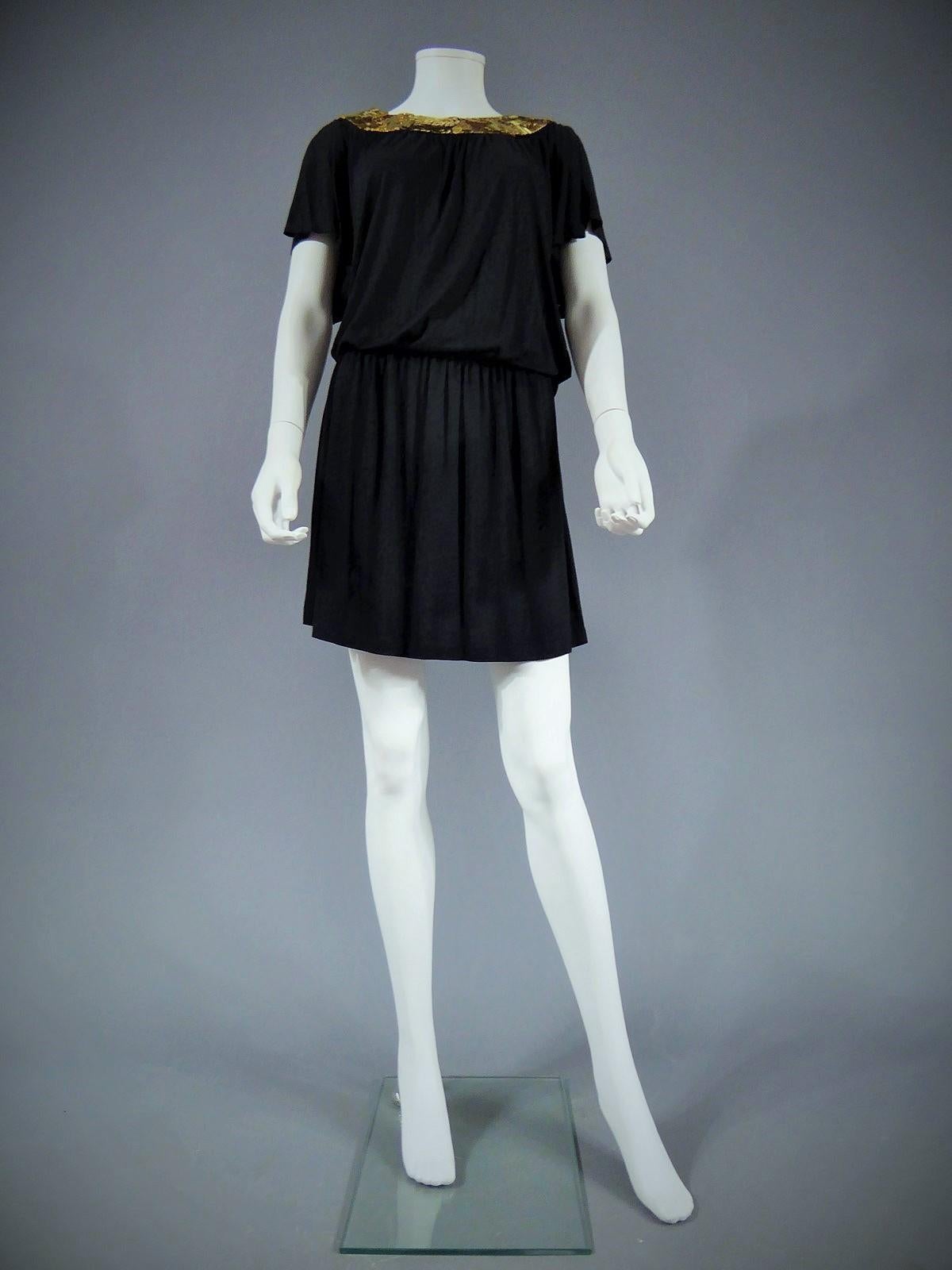 Circa 1970-1980

England.

Biba black mini dress and gold sequined collar. Opened on the back. Large and wide sleeves. Dress composed of a large t-shirt and a mini skirt, belt tight at waist. Zip closure on the skirt. Coton jersey. Biba was an