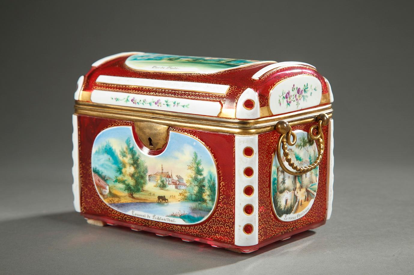 A rectangular casket in red  overlay glass mounted in gilded brass, decorated with polychromatic medallions with picturesque views of the German city Baden-Baden and with its tourist monuments: a panoramic view of the city on the lid, two sights of