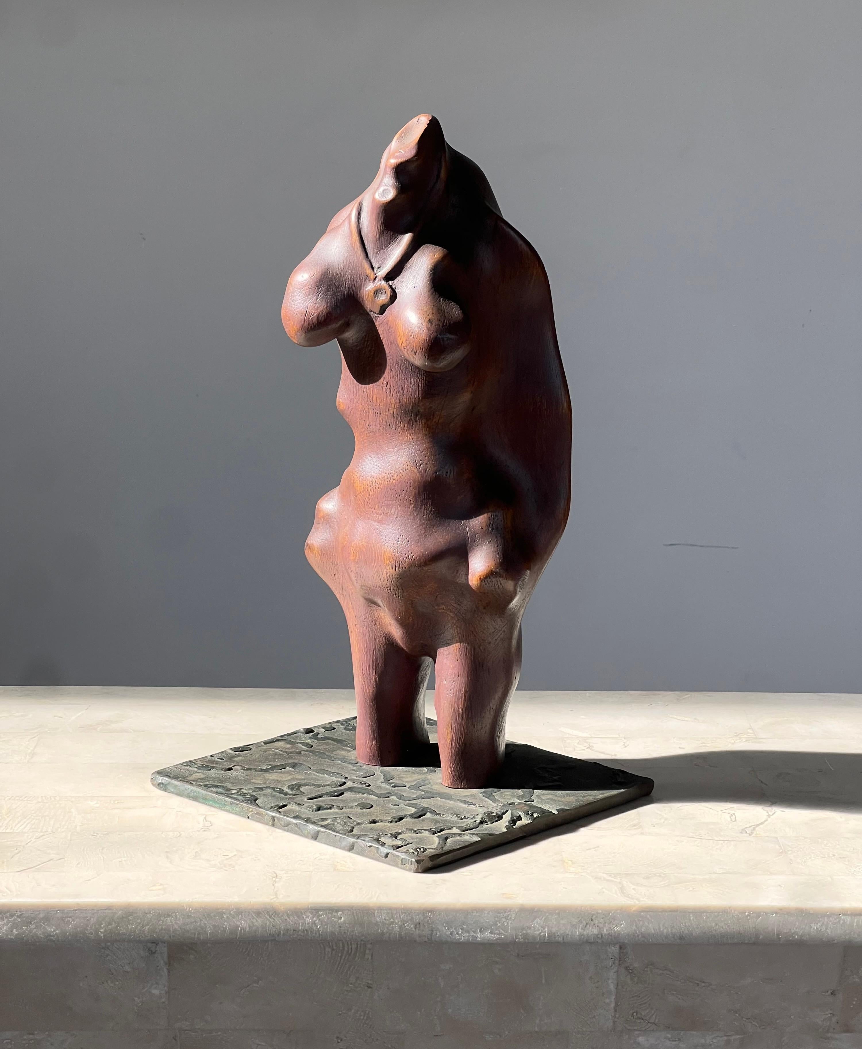 A biomorphic hand-carved sculpture of a femme, signed by artist, 20th century. In wood with hand-crafted embossed iron base. This piece is reminiscent of early Mesopotamian sculptures depicting women in various stages of fertility - notably pregnant