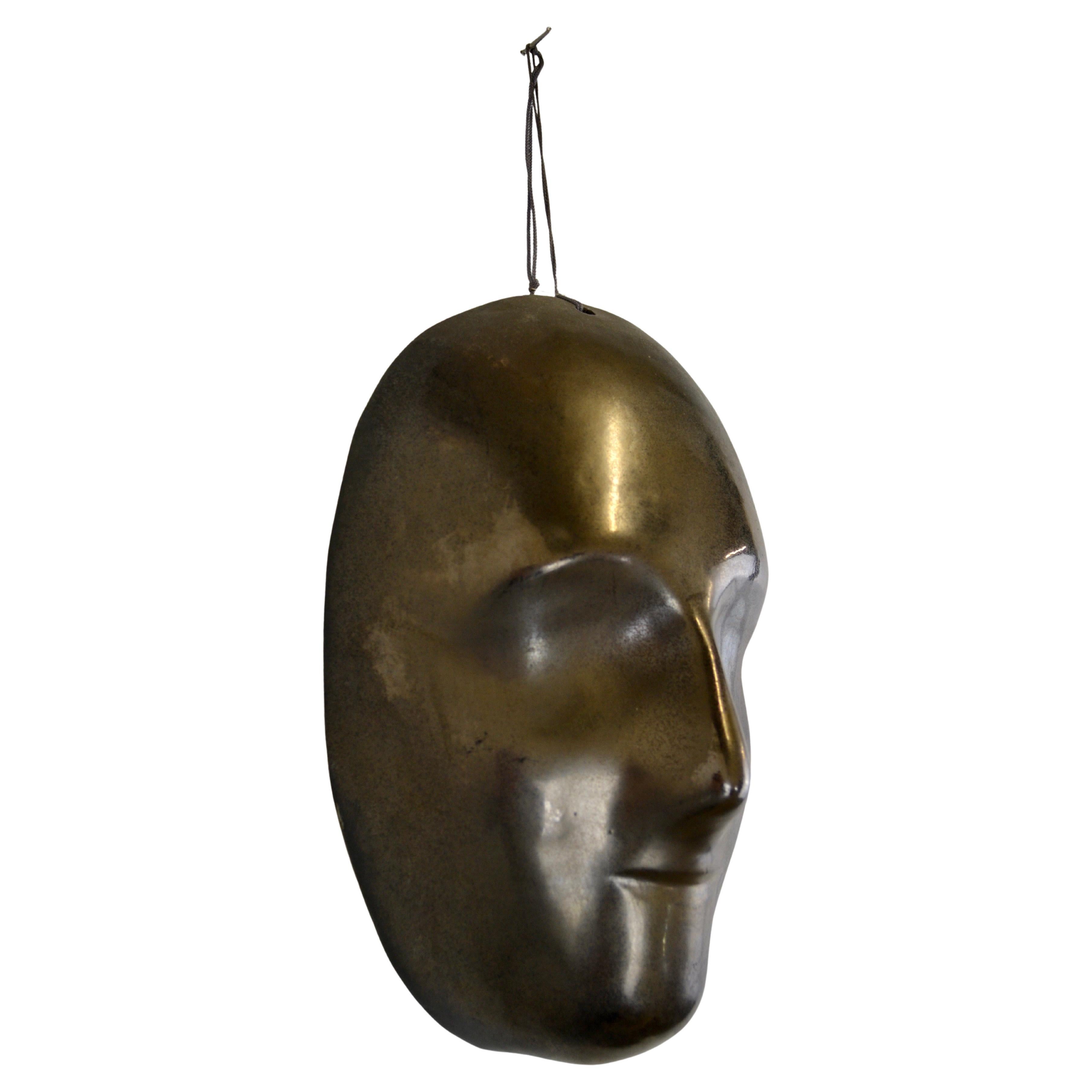 A striking black enamelled ceramic mask with shimmering bronze-gold highlights. This exceptional wall decor piece showcases the artistry of anonymous French craftsmanship from the 1950s.

