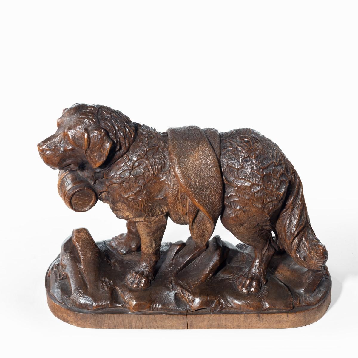 A ‘Black Forest’ carved linden wood model of a mount rescue dog, naturalistically modelled standing four-square with a barrel at his collar and a blanket wrapped around his middle, on an oval base carved with rocks and grasses. Swiss, circa