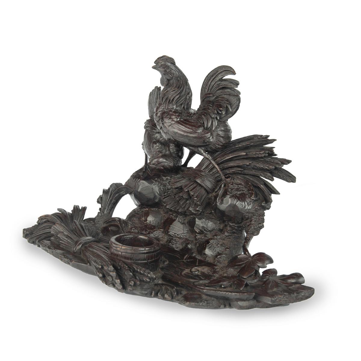 A Black Forest carved wood inkwell with wheat sheafs and poultry, made of ebonised fruitwood naturalistically carved with a cockerel and hen perched on a rocky outcrop, bundles of wheat, plants and a barrel in a stream. Swiss, circa 1890.
