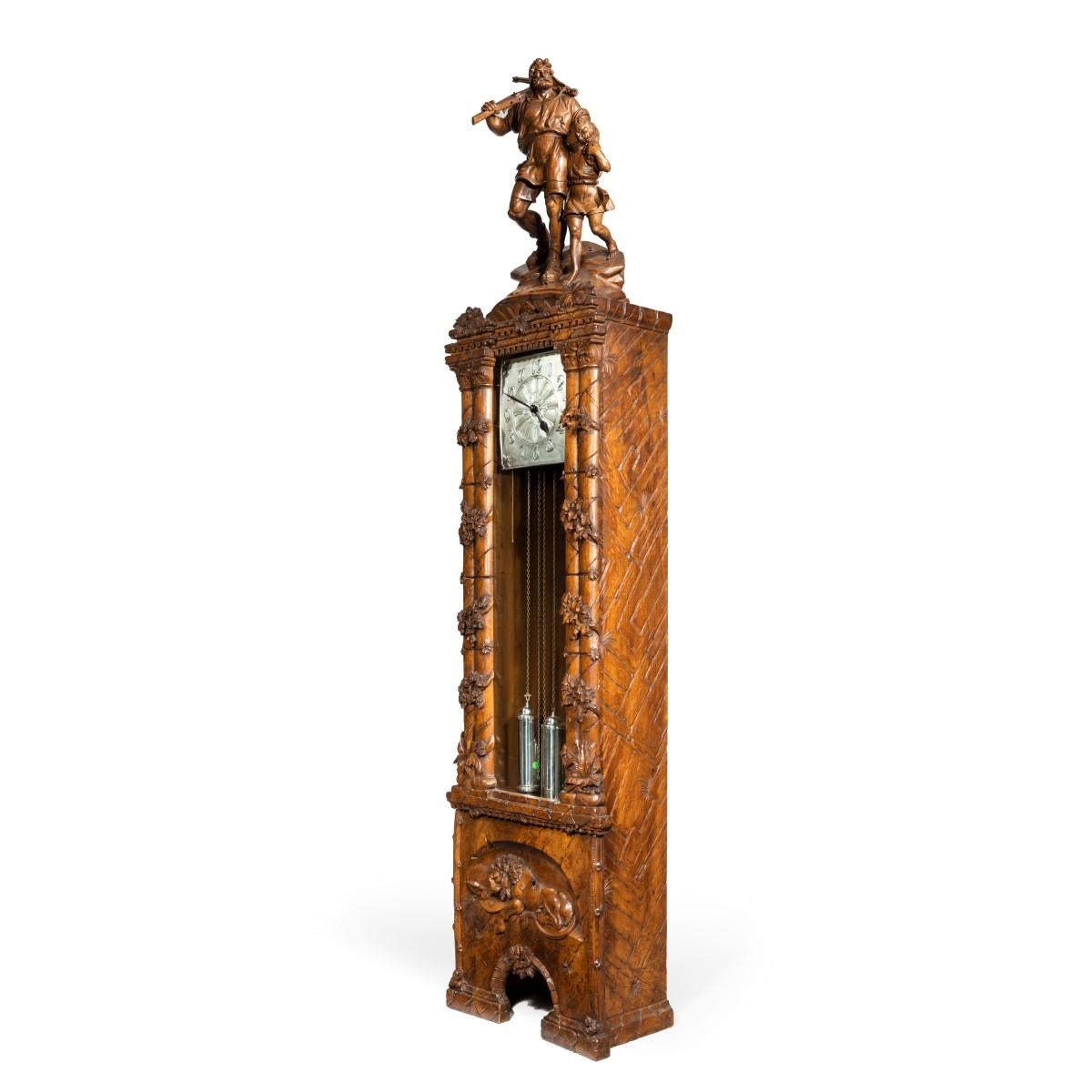 A ‘Black Forest’ linden wood long case clock by Spring of Interlaken, the square silvered dial enclosed behind a glazed door within an ornate case, surmounted by a carving of William Tell and his son after the “Tell Monument” by Richard Kissling