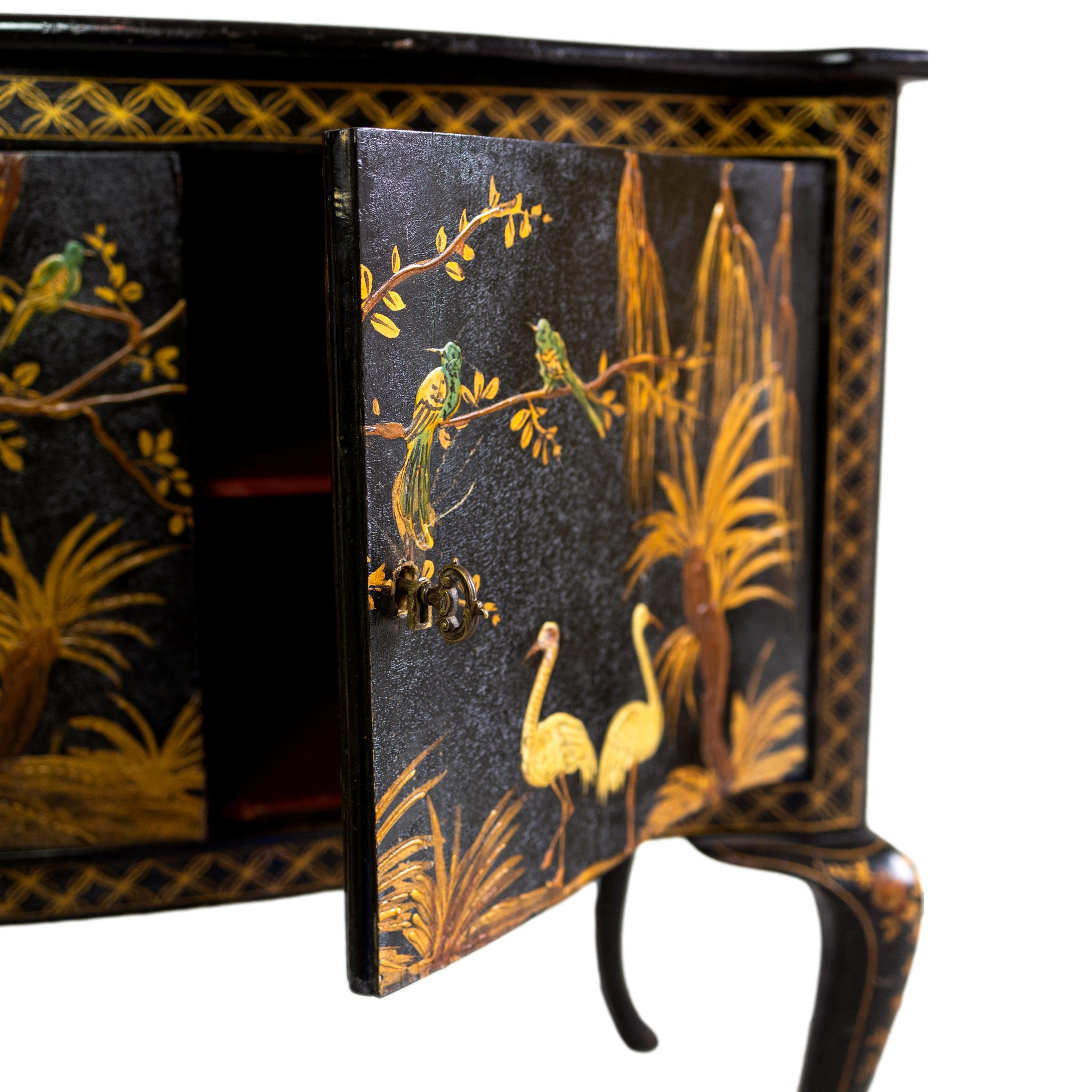 A Black Lacquered and Chinoiserie-Decorated Serpentine Cabinet, the top decorated with Chinese figures in a landscape, the two cabinet doors with a pair of cranes and bluebirds in a stylized landscape, the bowed sides similarly decorated, one with
