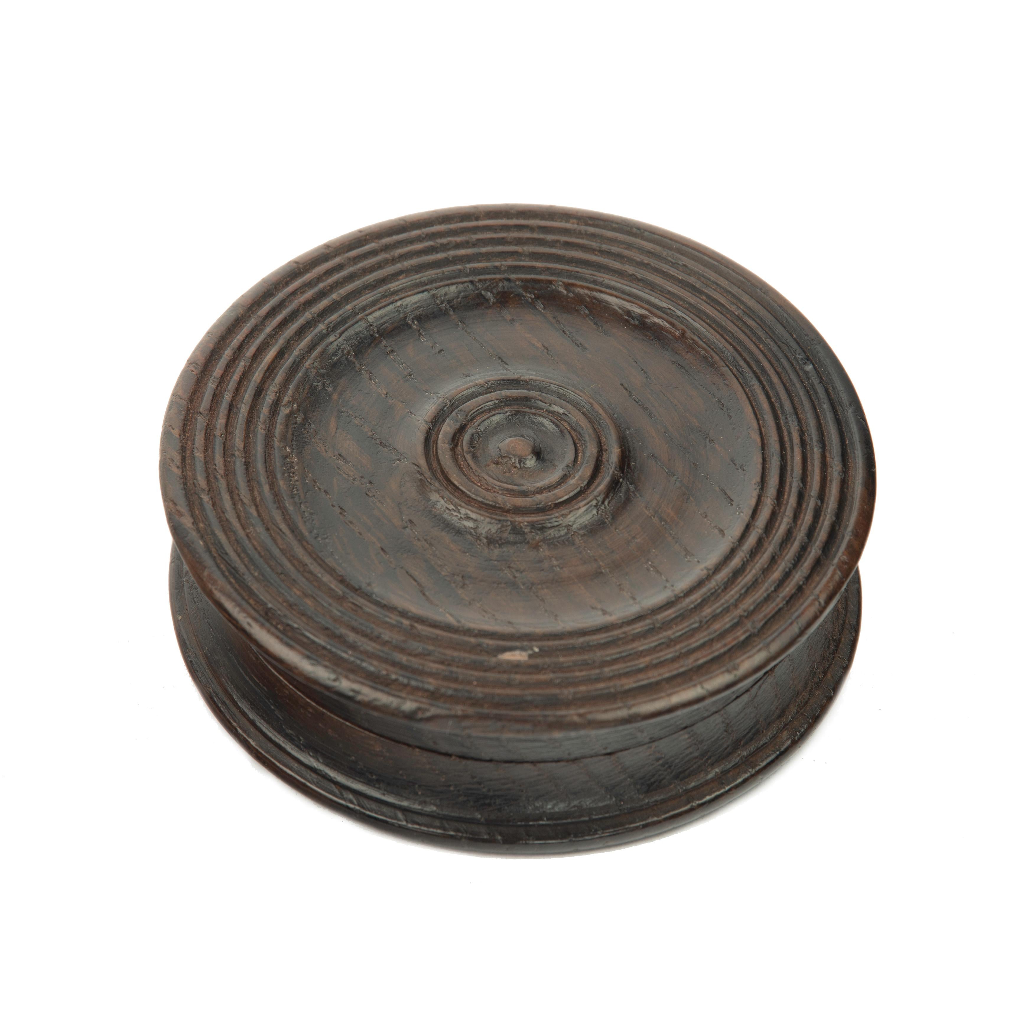A black oak snuff box made from timber recovered from H.M.S. Boyne, sunk 1795, raised 1833, of circular form with turned lid and base, the lid with printed description of Boyne’s career and sinking.  English, circa 1830. Diameter 3in. (7.5cm)
