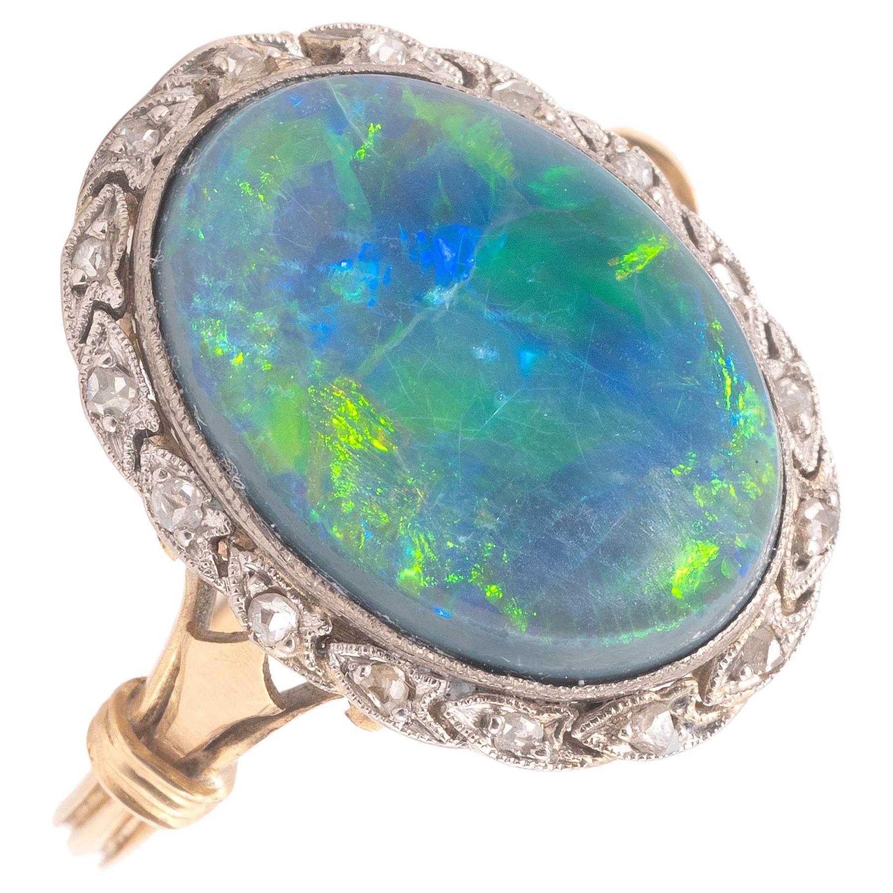 An opal and diamond cluster ring, the solid cabochon black opal claw-set within a single-cut diamond border, millegrain-set in platinum and yellow gold.

The oval cabochon-cut opal weighting approximately 8ct 

Size: 7
Weight: 5.56gr.

