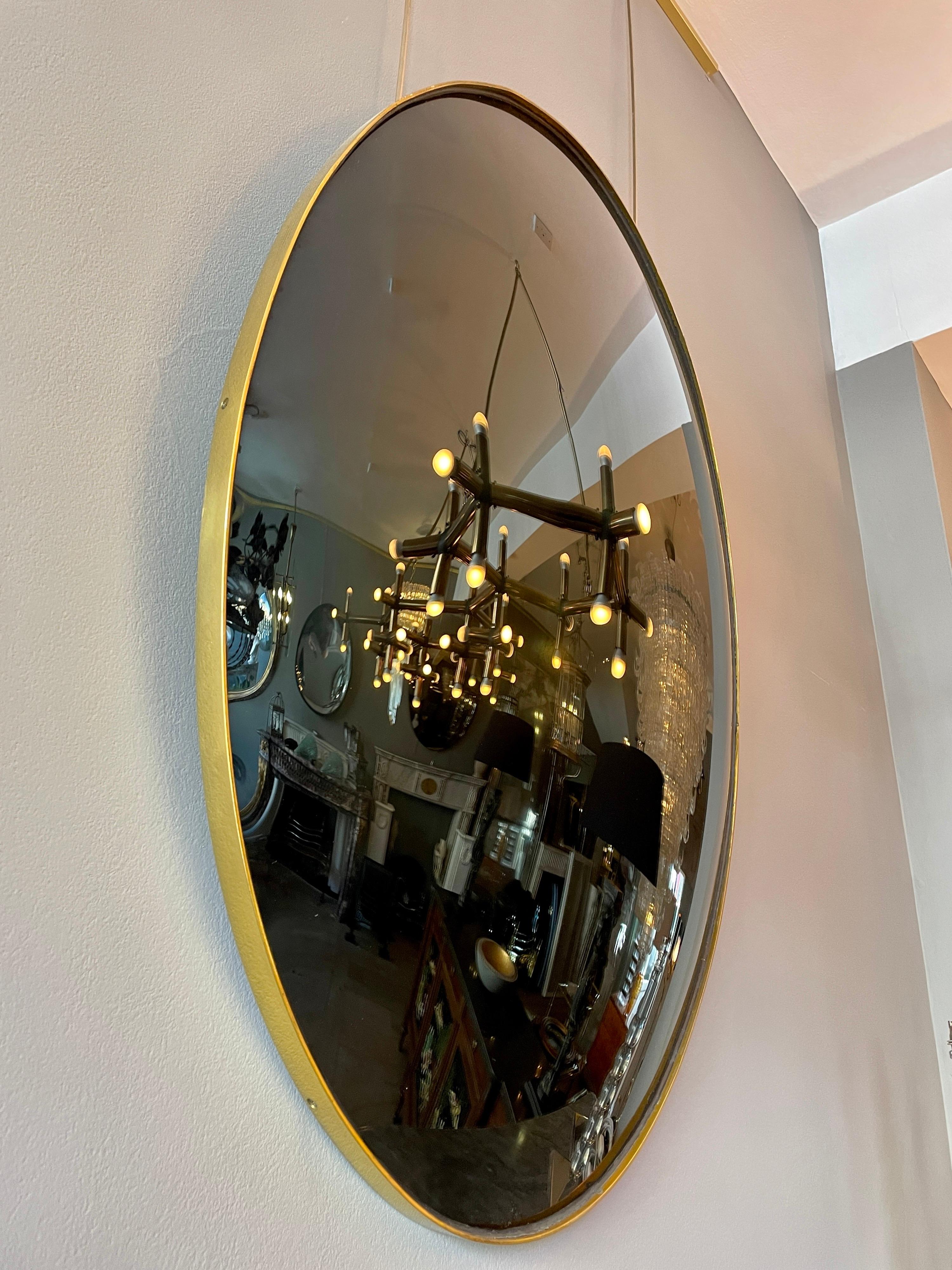 Un miroir ovale en verre convexe noir avec un cadre à bandes en laiton. Pièce contemporaine fabriquée au Royaume-Uni.
