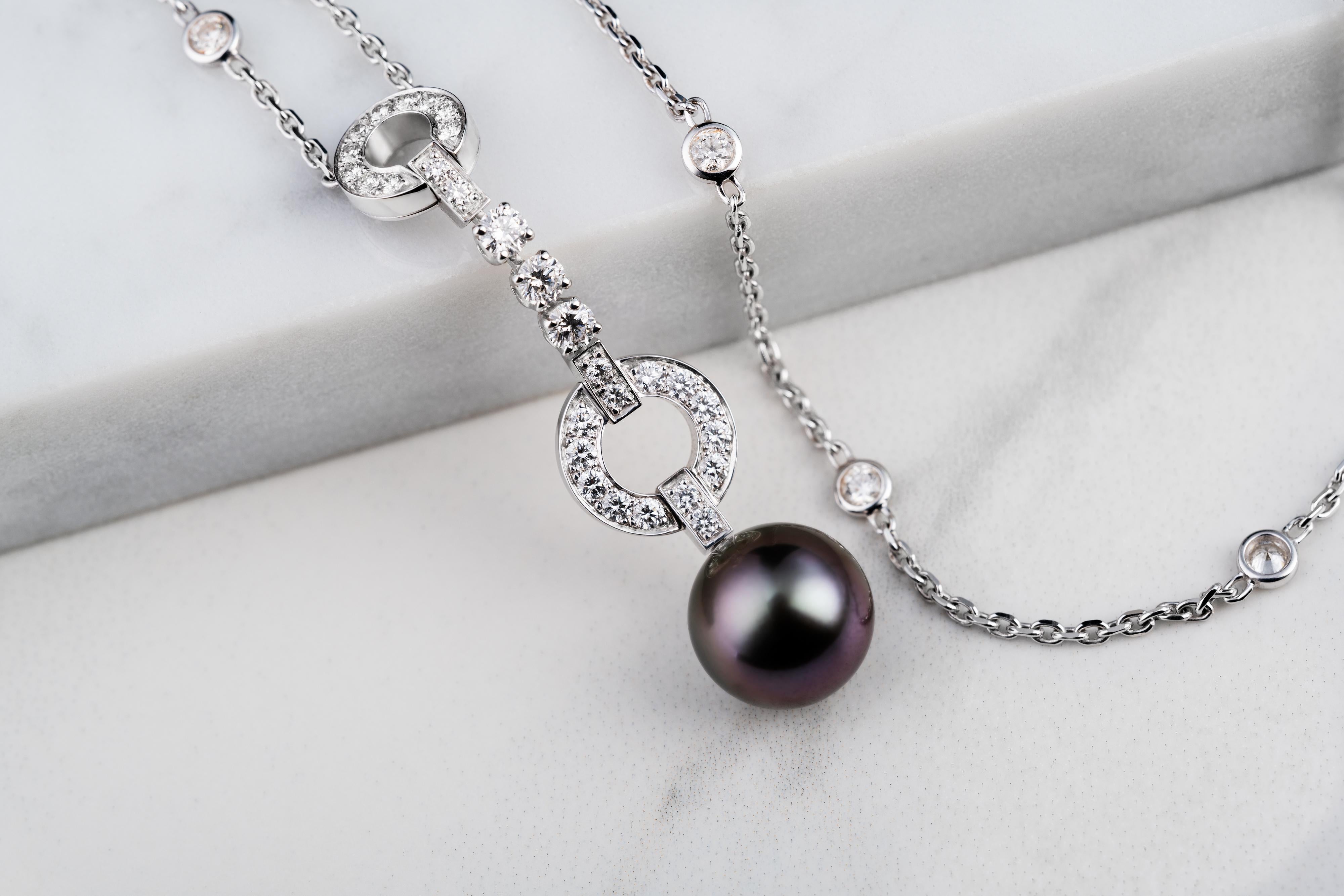 Featuring an oval cable chain with accents of bezel-set diamonds along the full length, leading perfectly to a unique geometric pattern of circles before a stunning black pearl drop. With shimmers of purple colours across its surface it is a