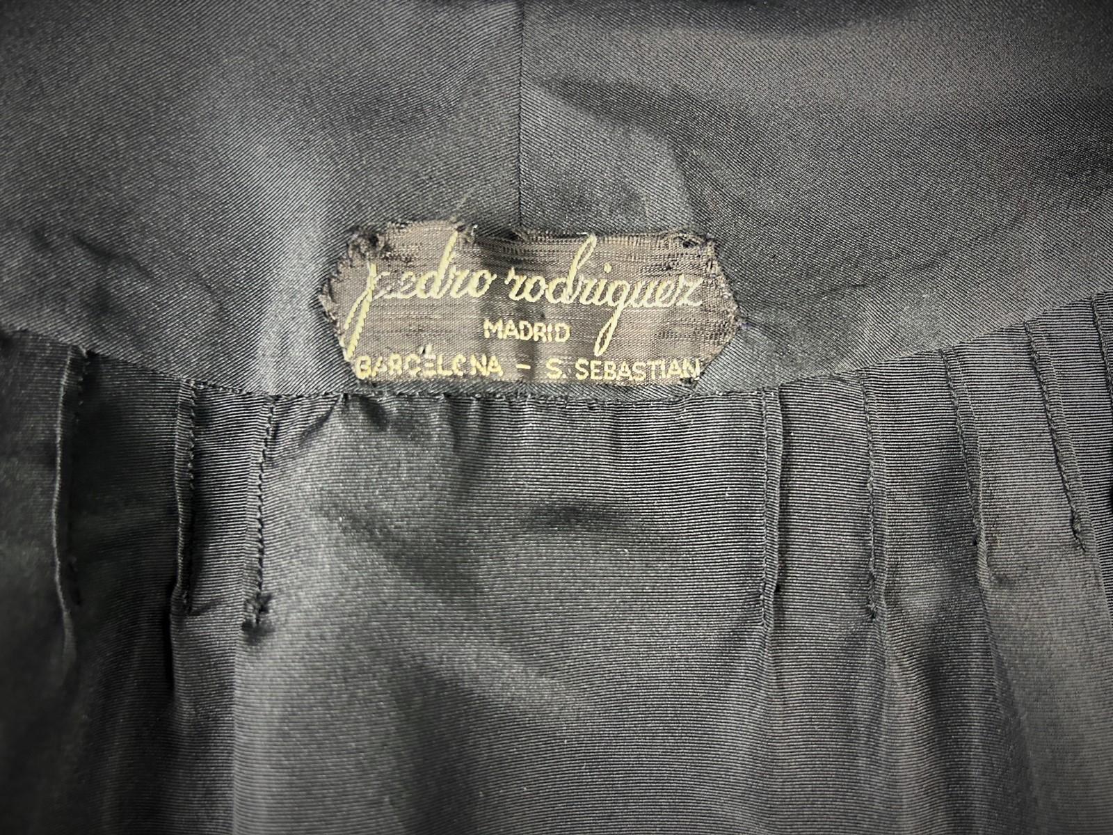 CIRCA 1955-1960
Spanien
Schwarzer Abendmantel aus Seidenfaille von Pedro Rodriguez, einem berühmten spanischen Couturier, aus den späten 1950er Jahren. Ein voller, ausgestellter Mantel mit einem auffälligen Rückenausschnitt, der sich an den Arbeiten