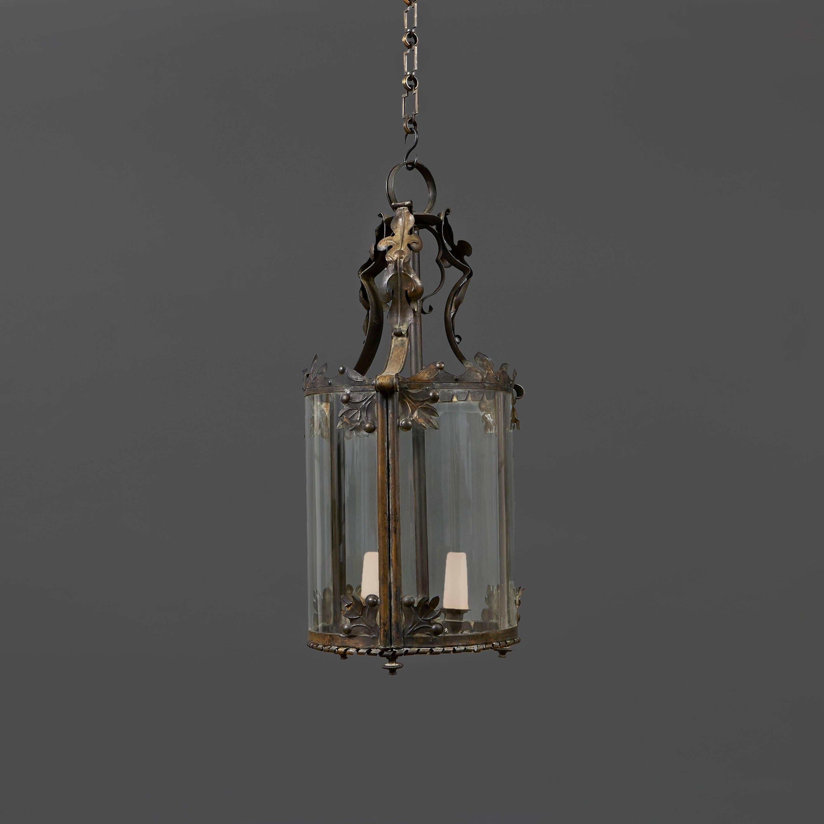England, circa 1890

A late nineteenth century toleware lantern, with foliate decoration throughout, the scrolling leaves to the top supporting a three candle arm lighting fitting within the curved glass body, the corners of the panels decorated
