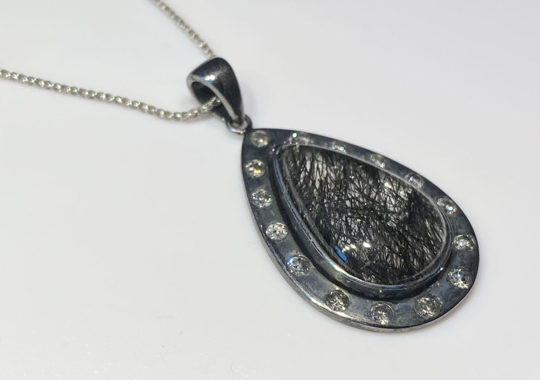 A Champagne Diamond & Quartz Cabochon Pendant, set in darkened Silver.
This Pendant features a central Pear shaped Graphitite Cabochon (Quartz with Graphite Needles) of 27 Carats, surrounded by 15 Round Diamonds which are SI quality and Tinted Grey.