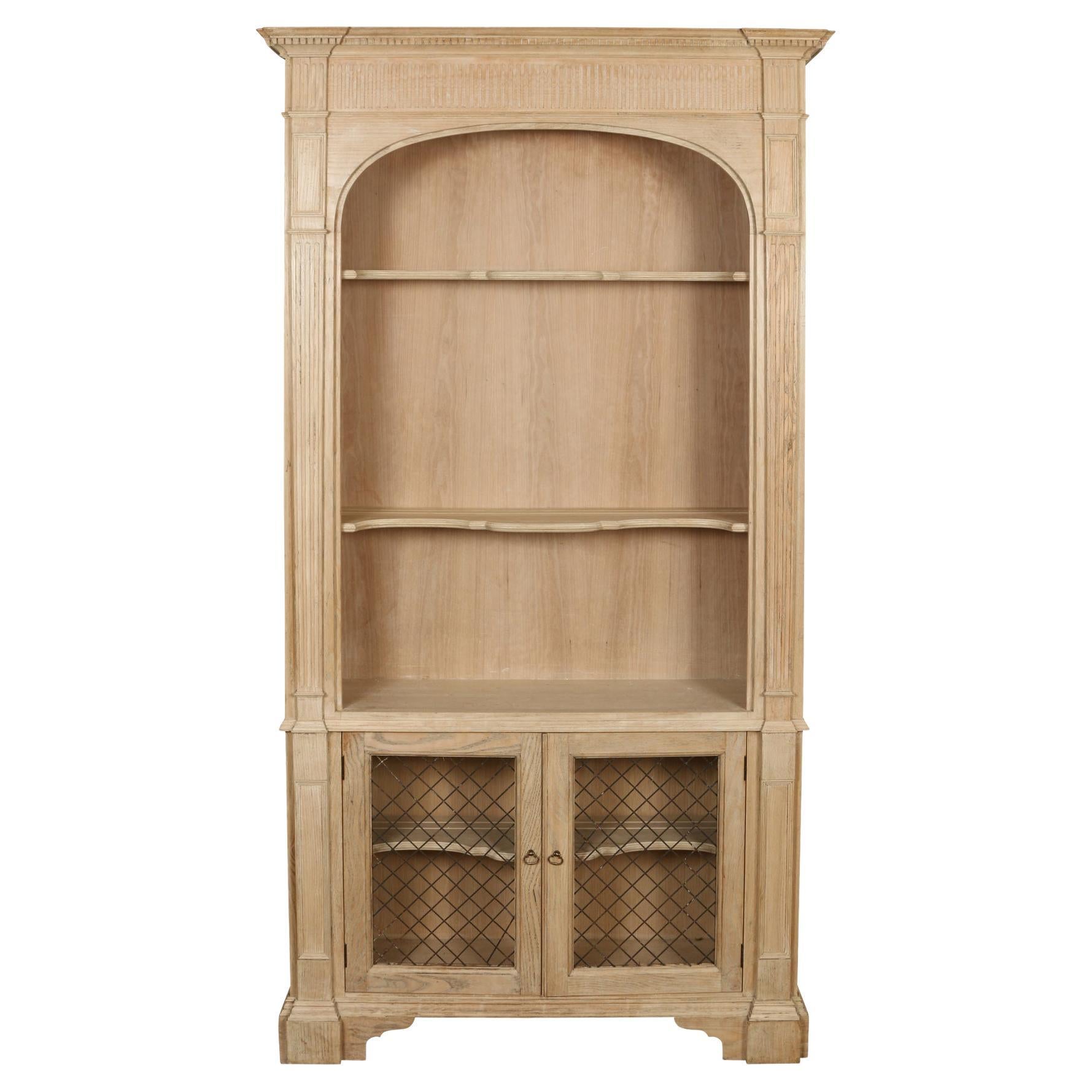 A handsome Baker bookcase in a bleached mahogany finish. The neoclassical style pieces feature two columns on either side and and a straight pediment with dental molding. This piece has three upper shelves, two with a scalloped edge. The lower