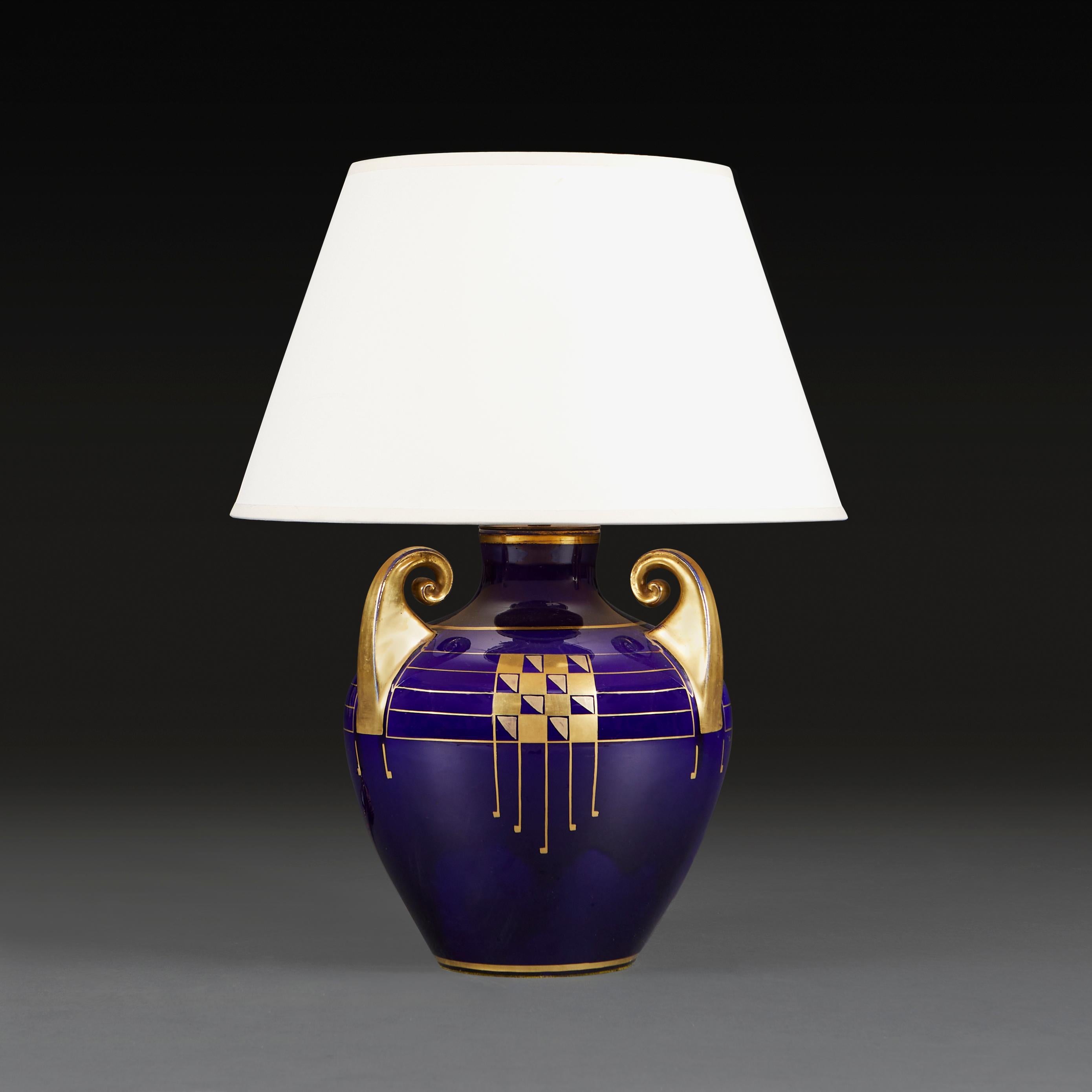 An Art Deco vase with royal blue glaze with overlaid geometric gilt decoration, of bulbous form with three scrolling handles, now as a lamp.
France, circa 1930.
Height of vase     28.00cm
Height with lampshade  53.00cm
Diameter of base  