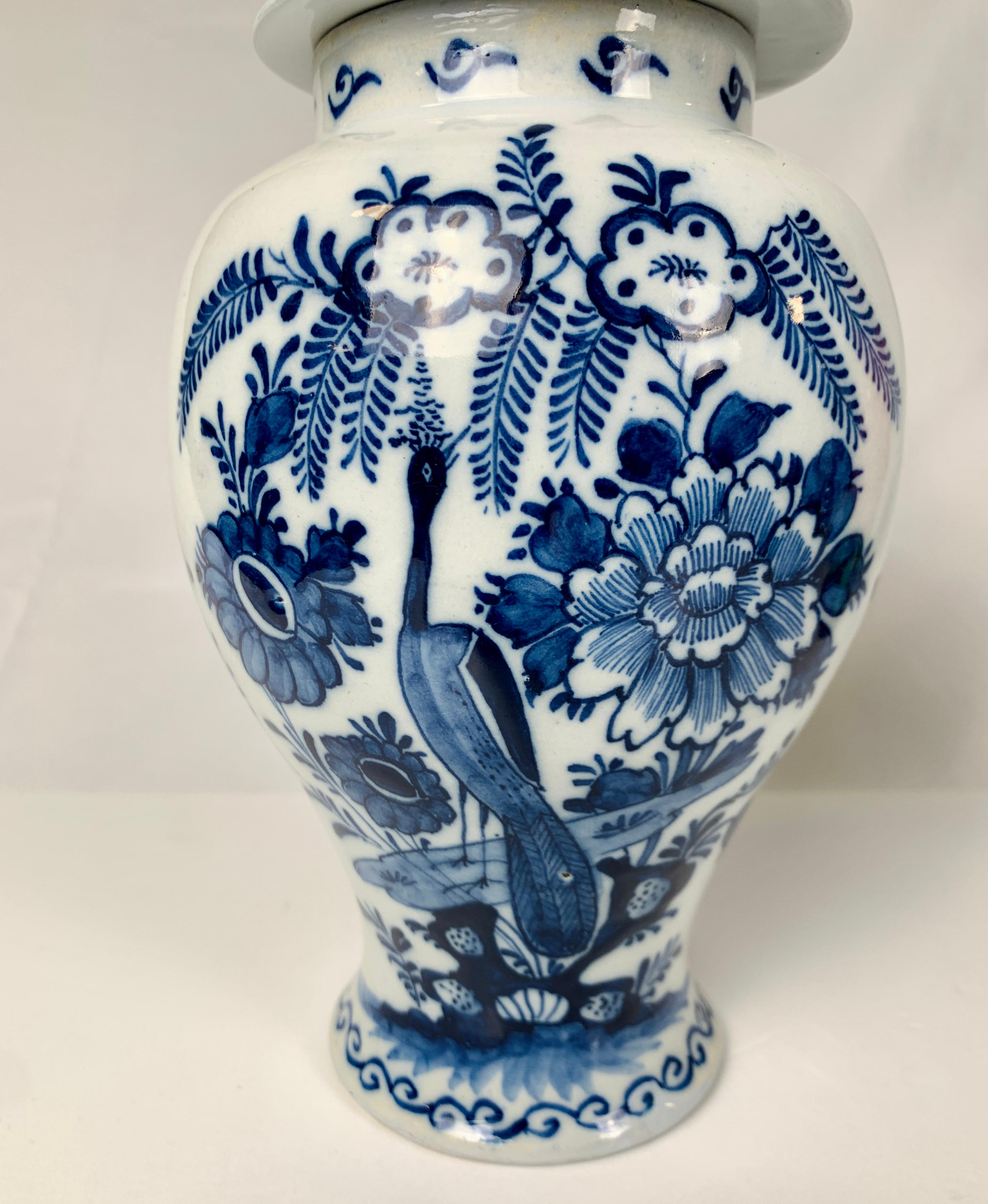 A blue and white Dutch Delft jar hand-painted in cobalt blue showing a peacock in a flower-filled garden.
The scene is inspired by Chinese porcelains of the 17th and 18th centuries.
The matching cover is decorated with flowers, ferns, and