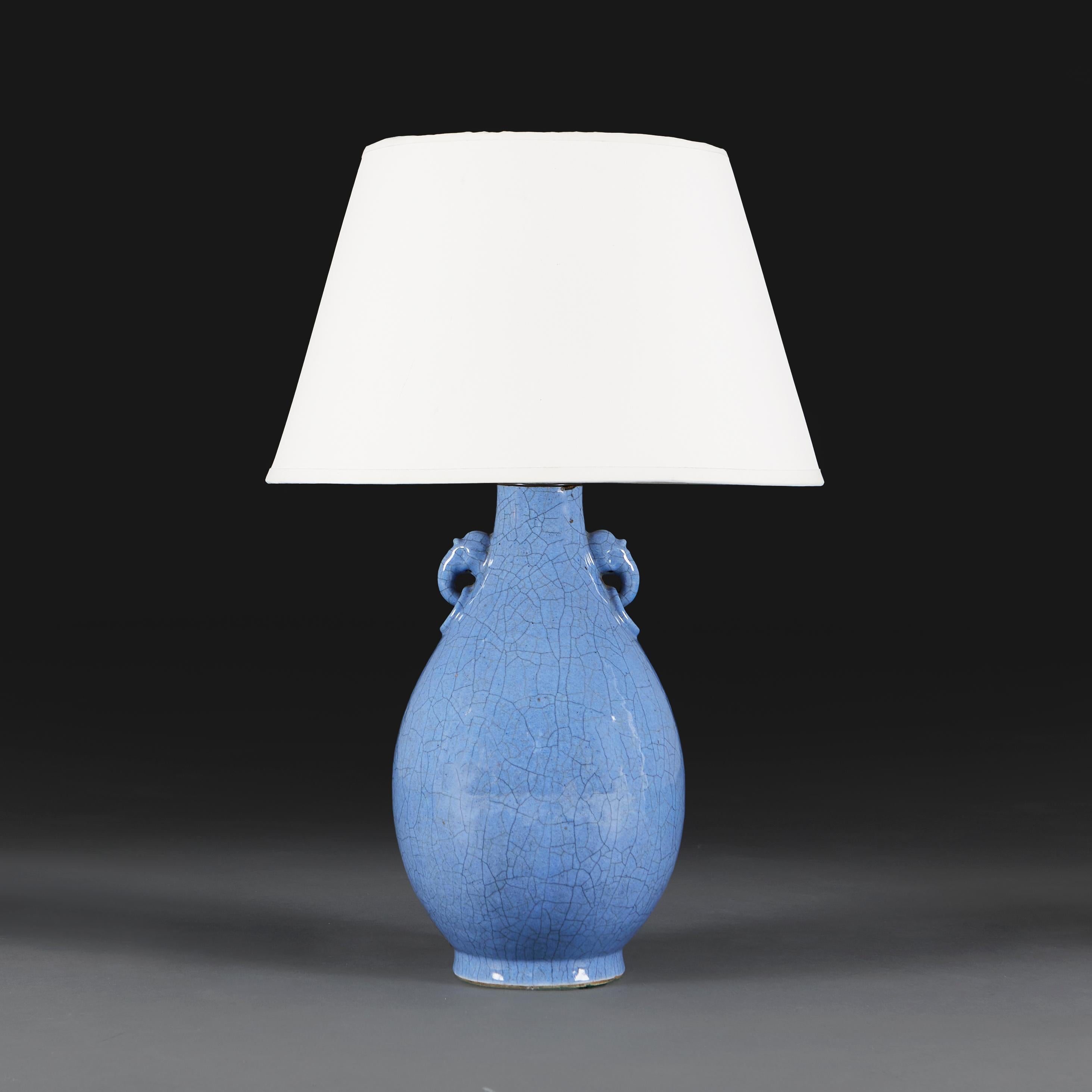 Un vase du vingtième siècle à glaçure craquelée bleu clair, avec des poignées en forme de masque d'éléphant au niveau du col, aujourd'hui converti en lampe.

Hauteur du vase   37.00cm
Hauteur avec abat-jour   62.00cm
Diamètre de la base  