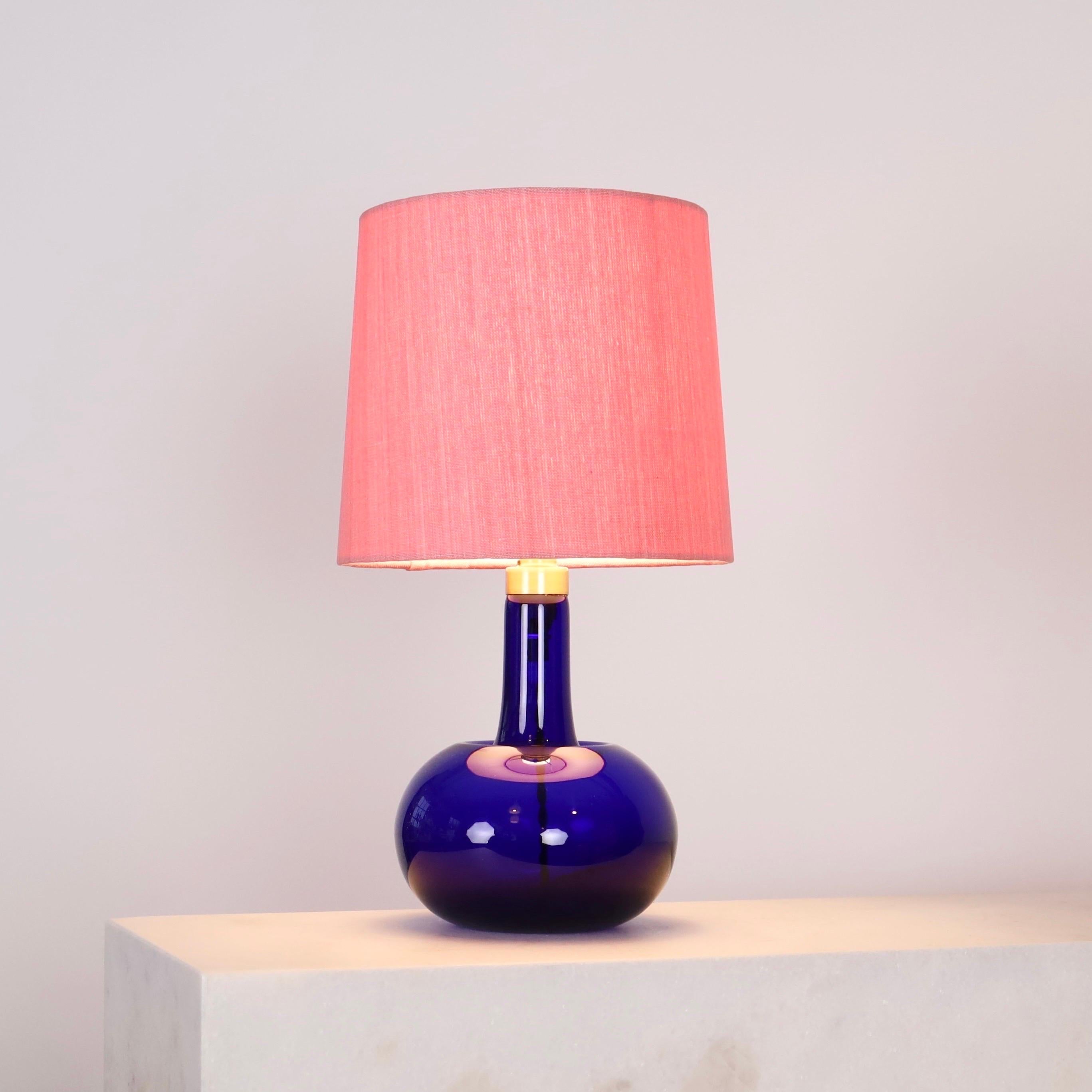 A blue desk lamp designed by Michael Bang for Danish Holmegaard Glasværk in 1975 accomplished new a shade made of artisan textile from Mallorca. A colorful attribution to the a modern interior.

* A blue glass table lamp with brass neck and a pink